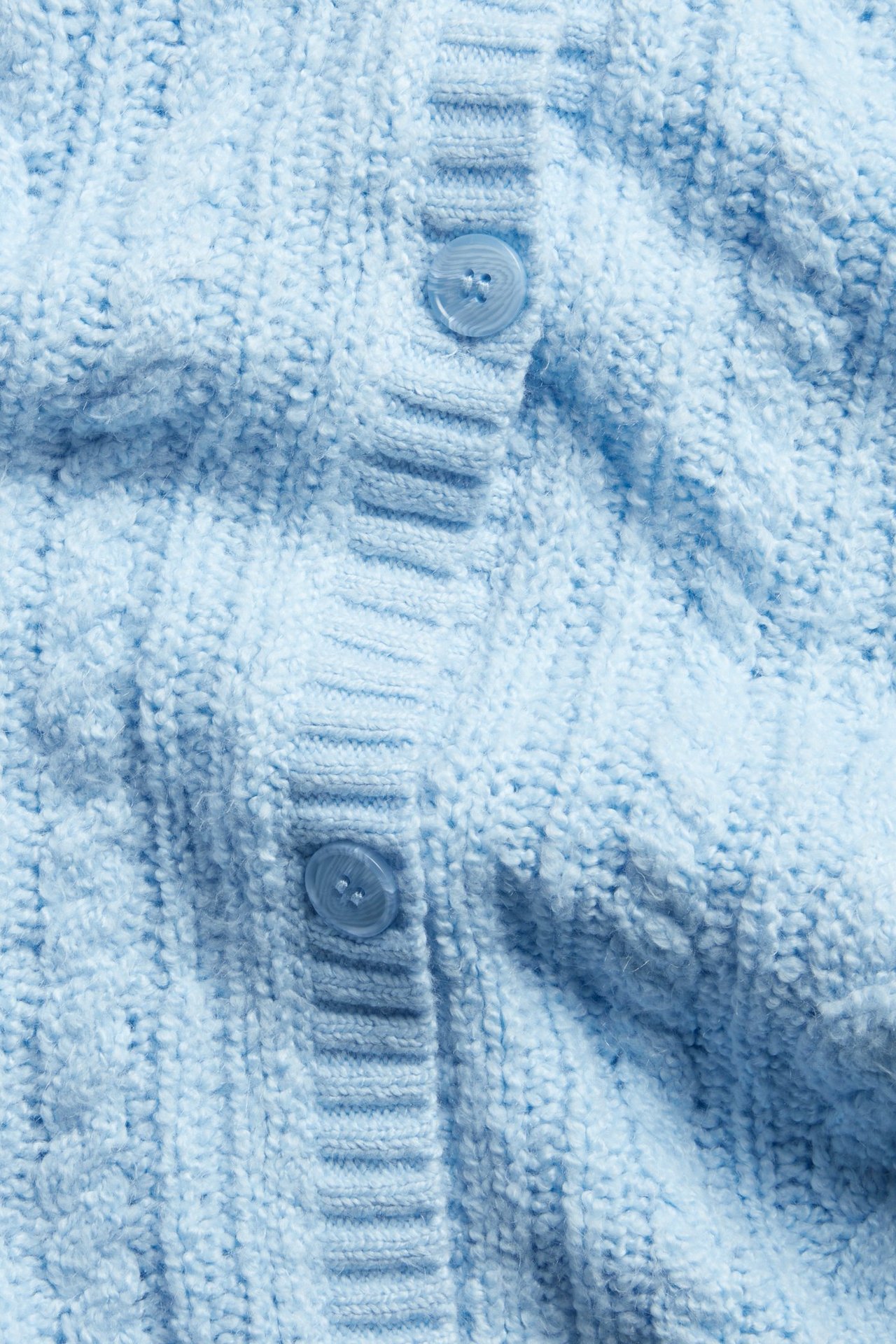 Zbliżenie na jasnoniebieski kardigan ze splotem warkoczowym i dwoma guzikami z przodu.
