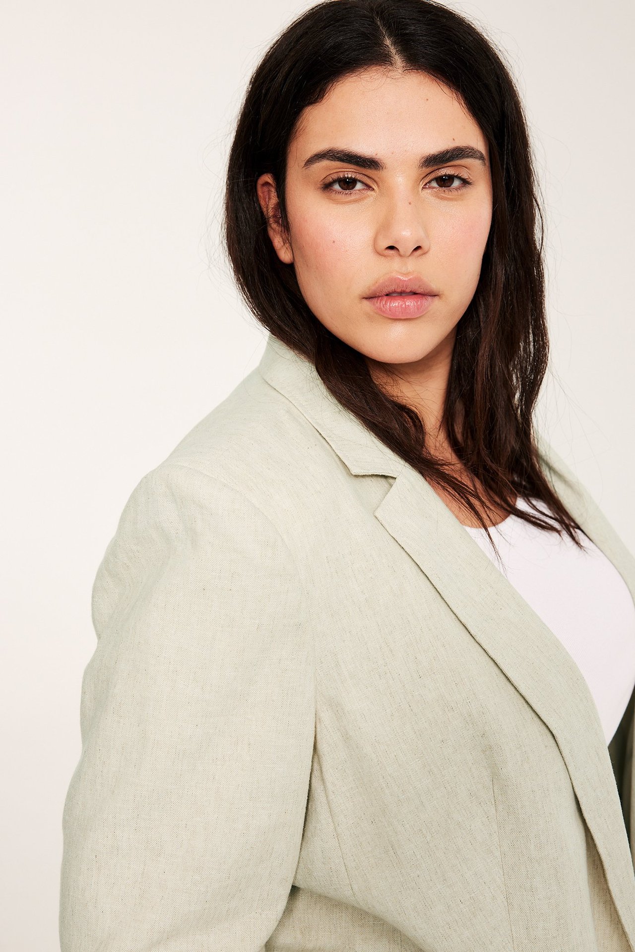 Zbliżenie z przodu kobiety w jasnobeżowym melanżowym żakiecie z domieszką lnu na białym topie.