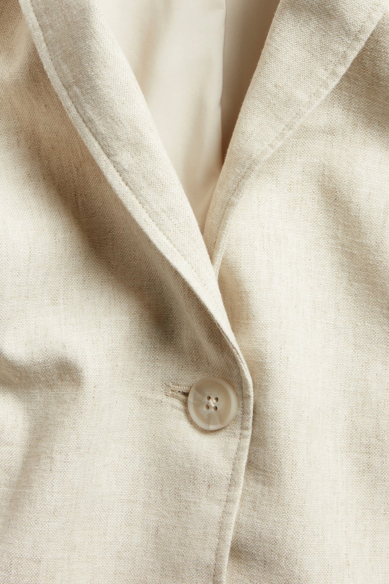 Zbliżenie z przodu beżowej melanżowej jednorzędowej marynarki z mieszanki lnu z jasnym guzikiem.