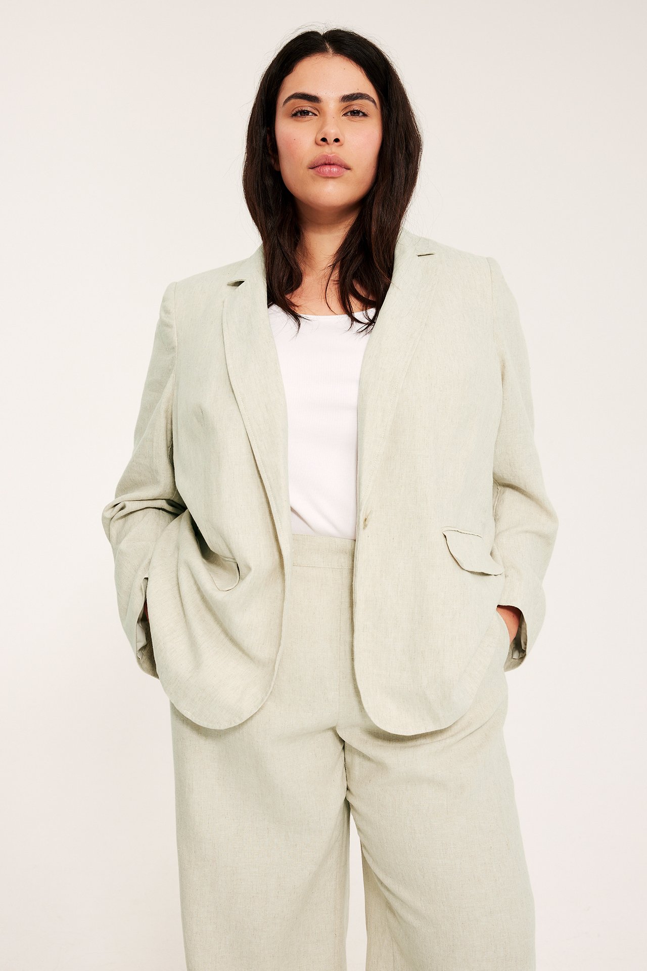 Edestä, nainen avoimessa beigenmelange pellavasekoitekavajassa, valkoisen topin ja yhteensopivien housujen kanssa.