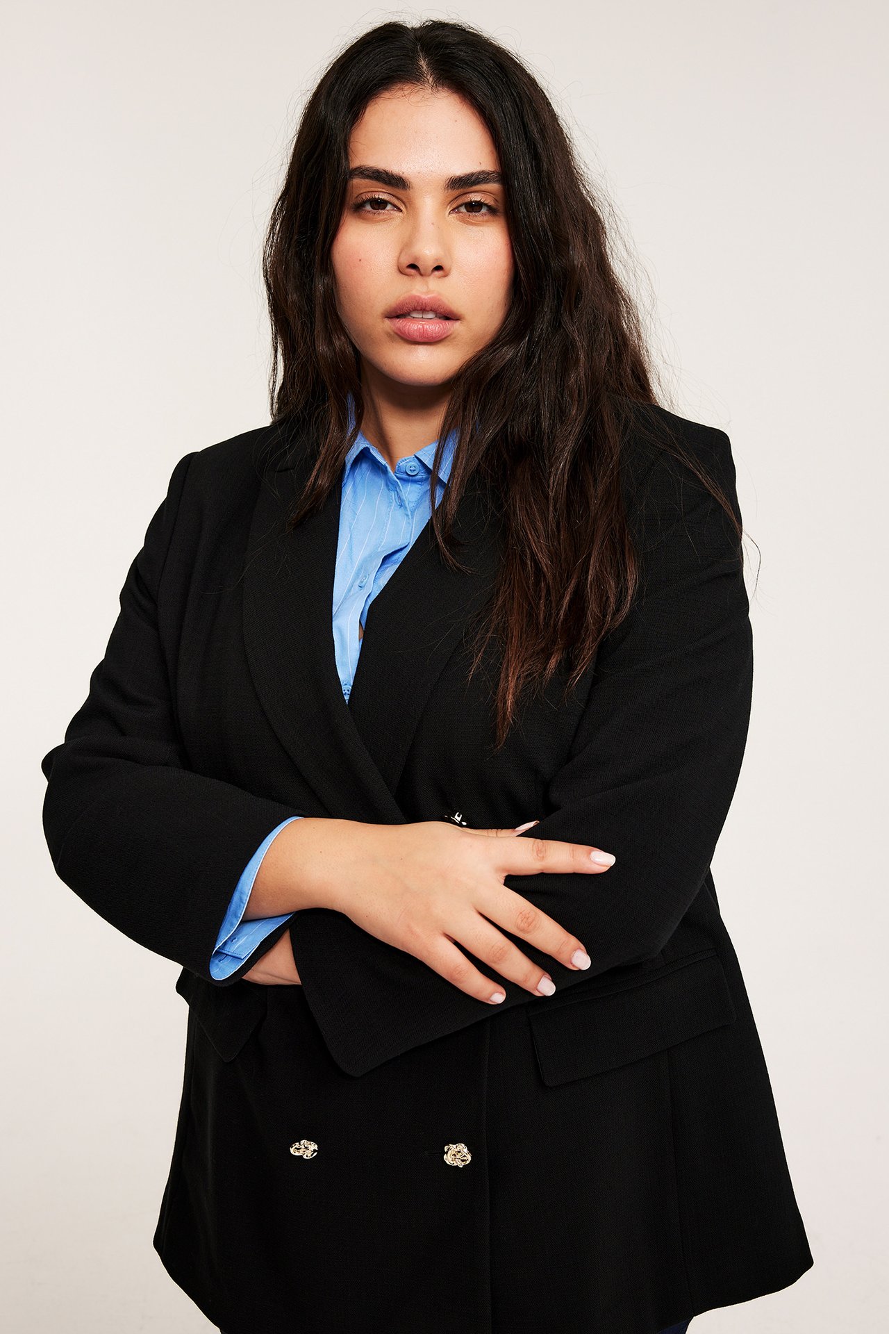 Nainen edestä, yllään musta kaksirivinen bleiseri kultanapeilla sinisen raidallisen paidan päällä.