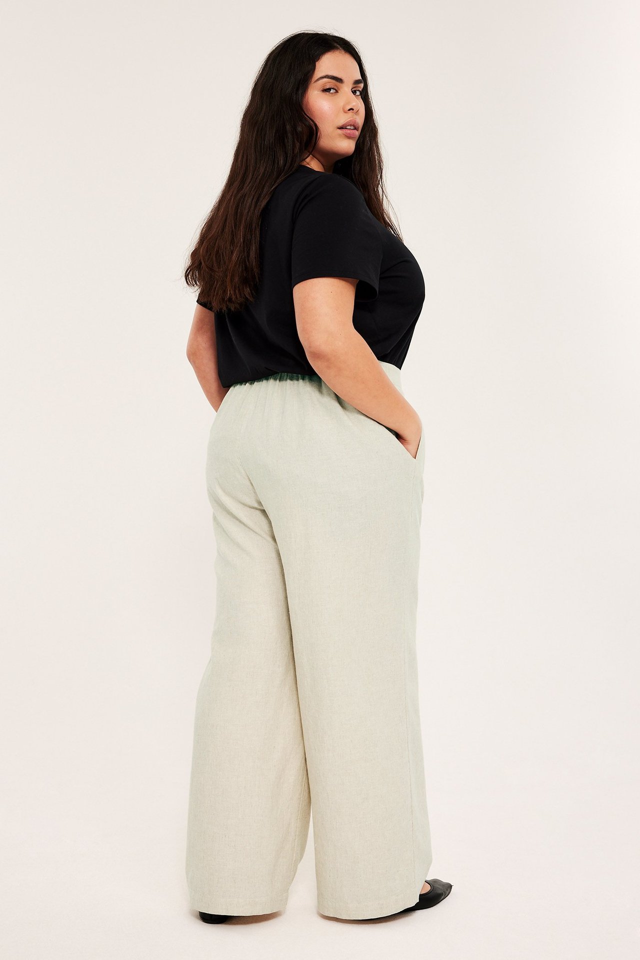 Sidovy: Kvinna i beigemelerade, avslappnade pull on-byxor i linnemix, svart t-shirt och svarta platta skor.