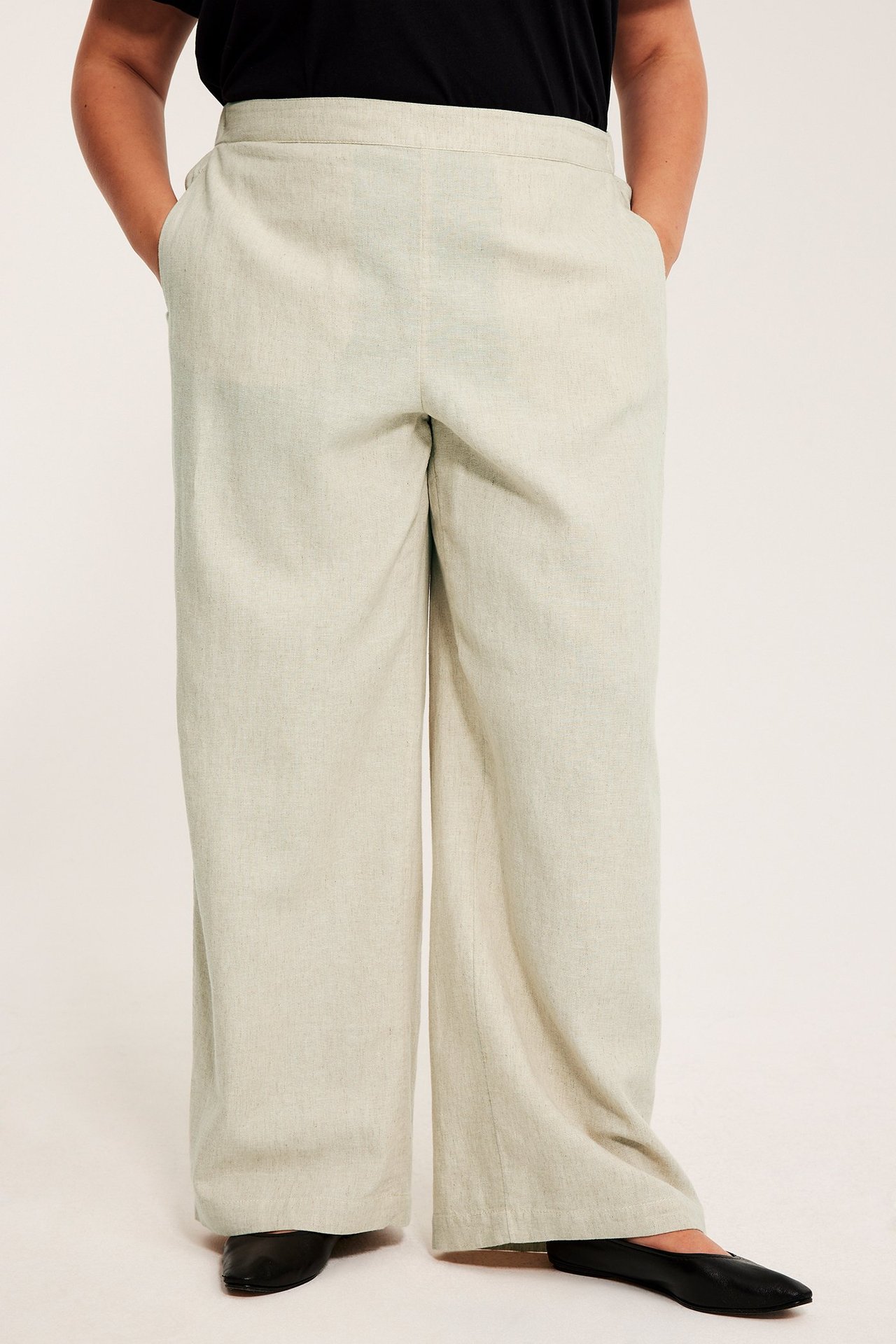 Widok z przodu: Kobieta w luźnych beżowych spodniach pull-on z lnu, z kieszeniami i czarnym topem.