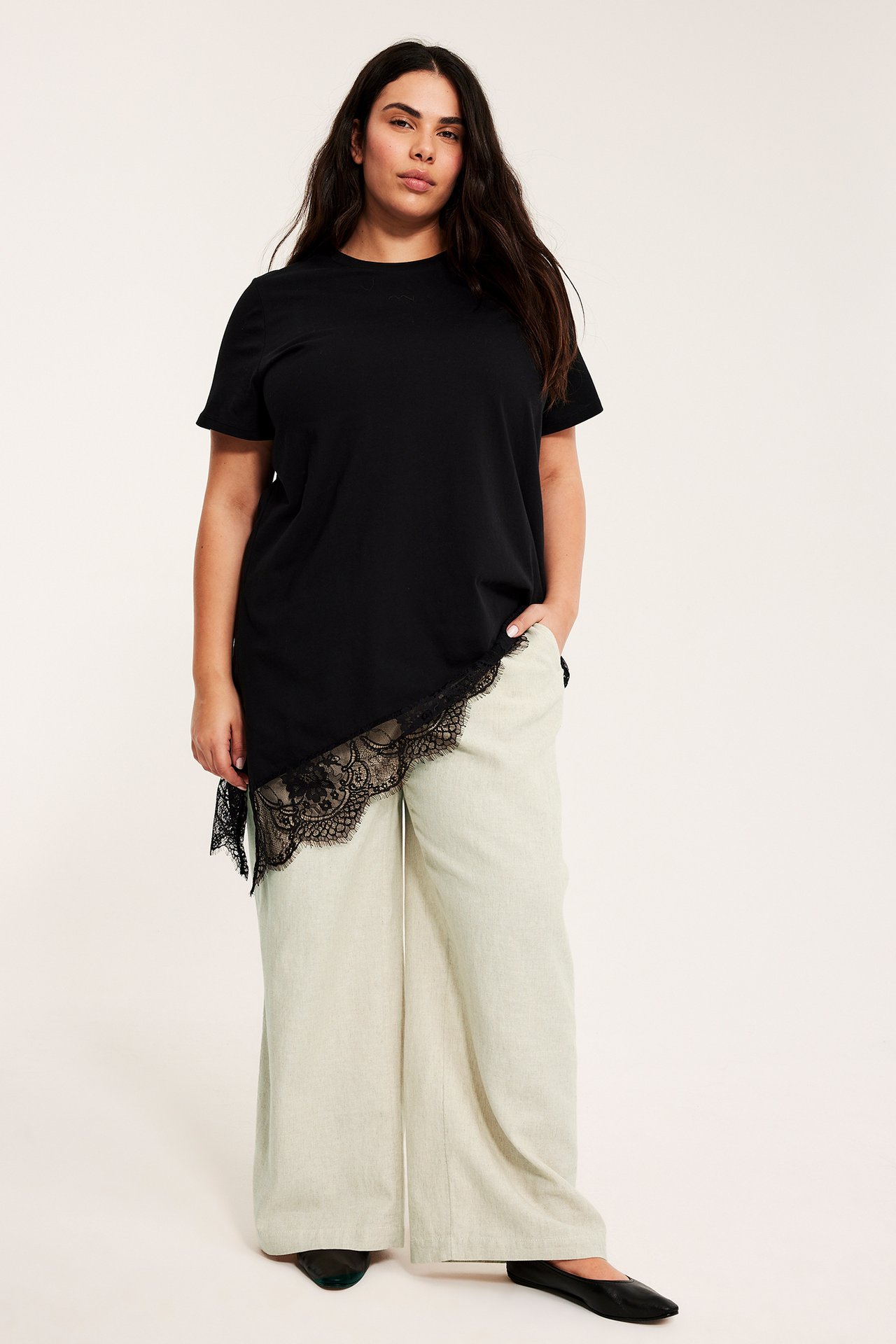 Etunäkymä: Nainen yllään meleroidut beiget pellavasekoitevetohousut, musta pitsit-paita ja mustat ballerinat.