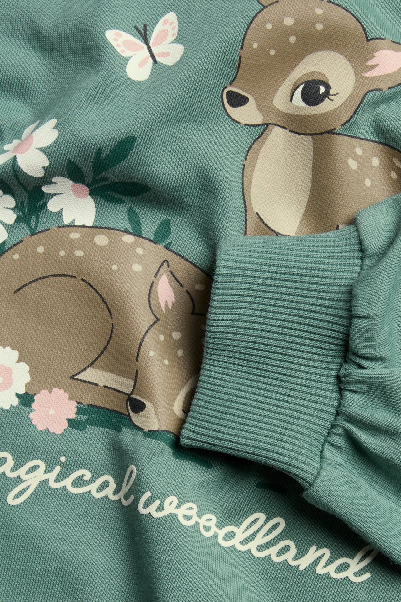 Zbliżenie na zieloną bawełnianą bluzę dziecięcą z nadrukiem saren, motyla i kwiatów.