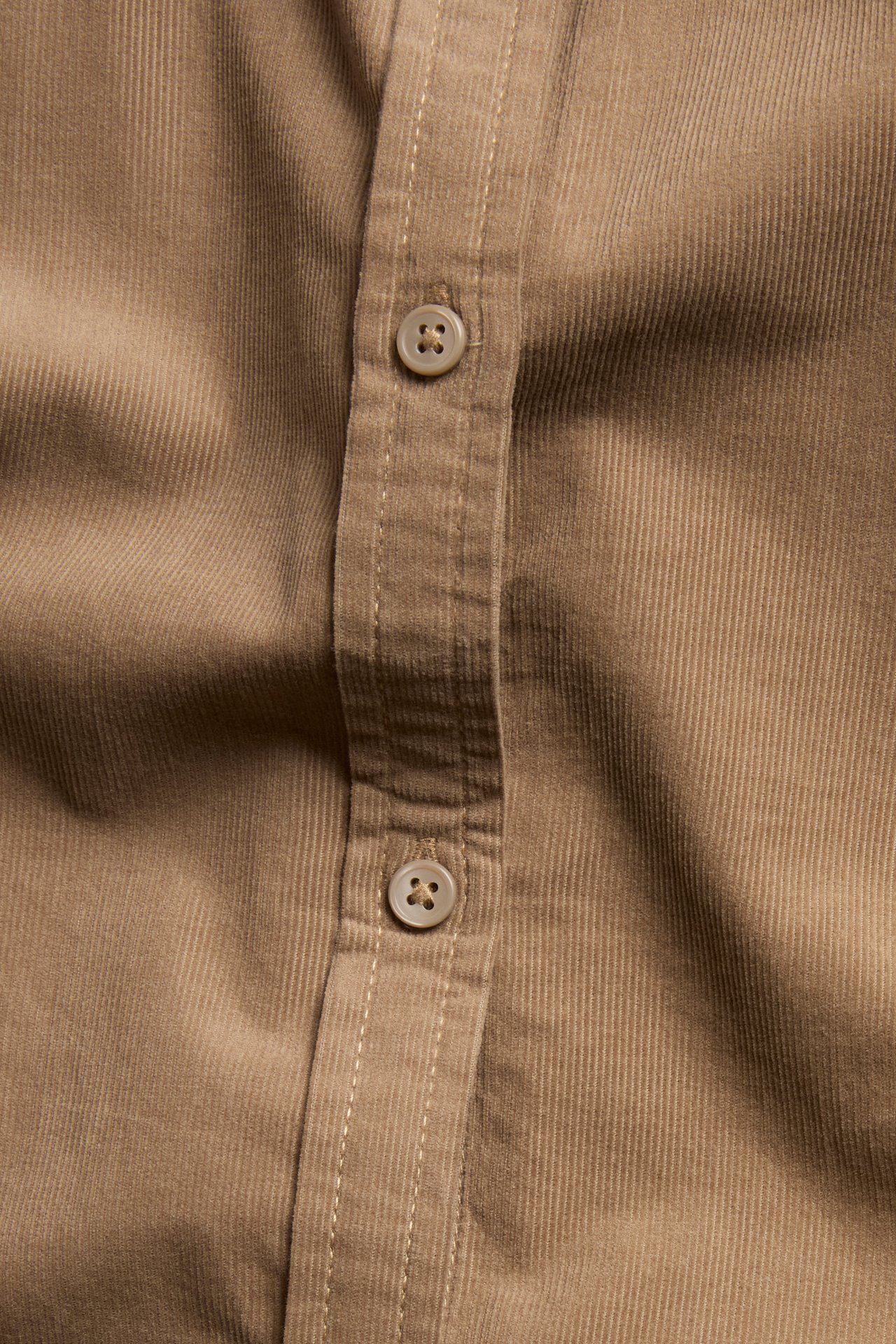 Zbliżenie na brązową sztruksową sukienkę koszulową z listwą guzikową i widocznymi guzikami.