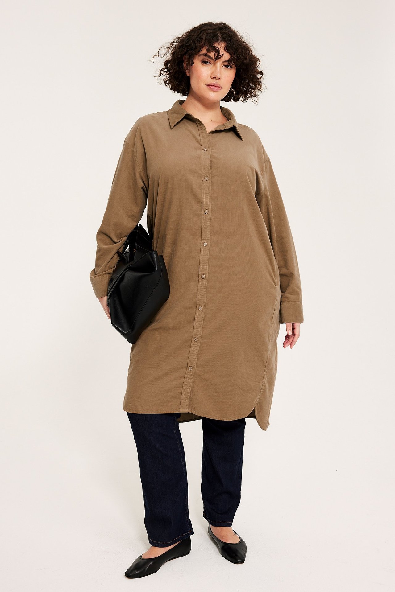 Edestäpäin: nainen ruskeassa vakosamettipaitamekossa, tummissa farkuissa, mustissa kengissä, musta laukku.