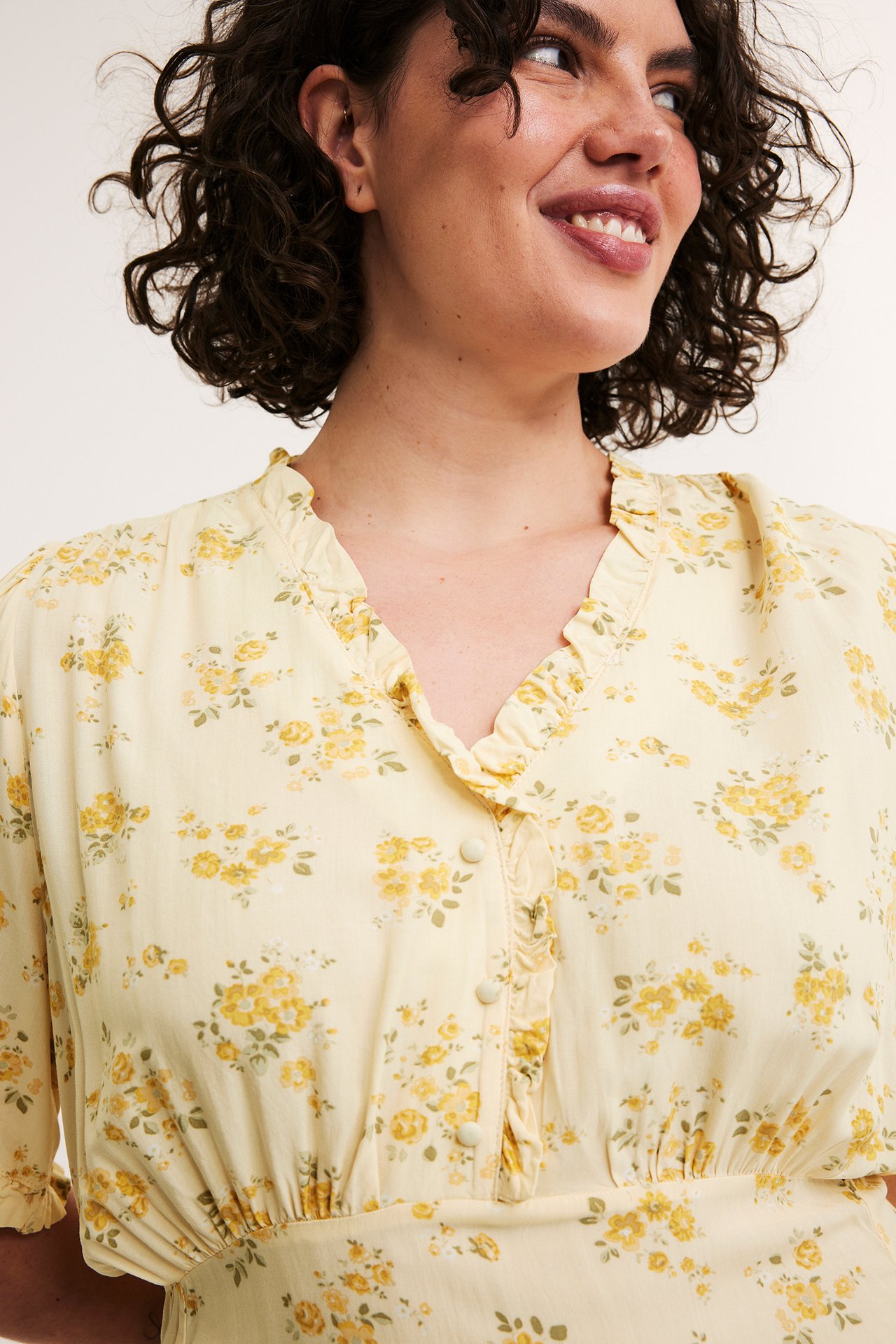Närbild av kvinna i ljusgul mönstrad viskosklänning med volang-V-hals och täckta knappar.