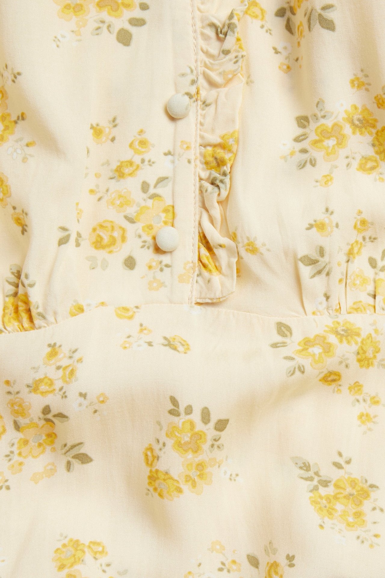 Lähikuva vaaleankeltaisesta viskoosimekostä, kukkakuosi, röyhelöt ja päällystetyt napit V-pääntiellä.