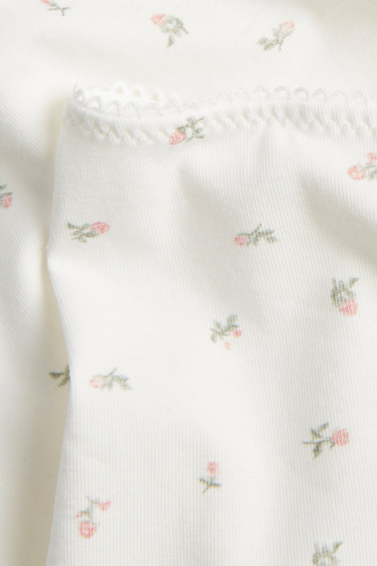 Zbliżenie na kremowe majtki z małym różowym kwiatowym wzorem i delikatną koronką.