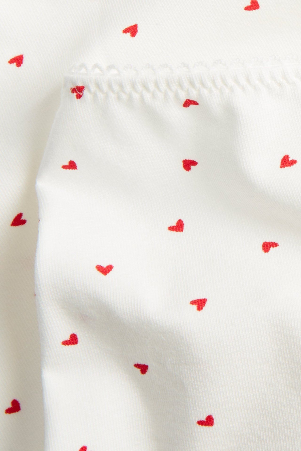 Närbild av offwhite brief-trosor i bomullsmix med rött hjärtmönster och resårkant.