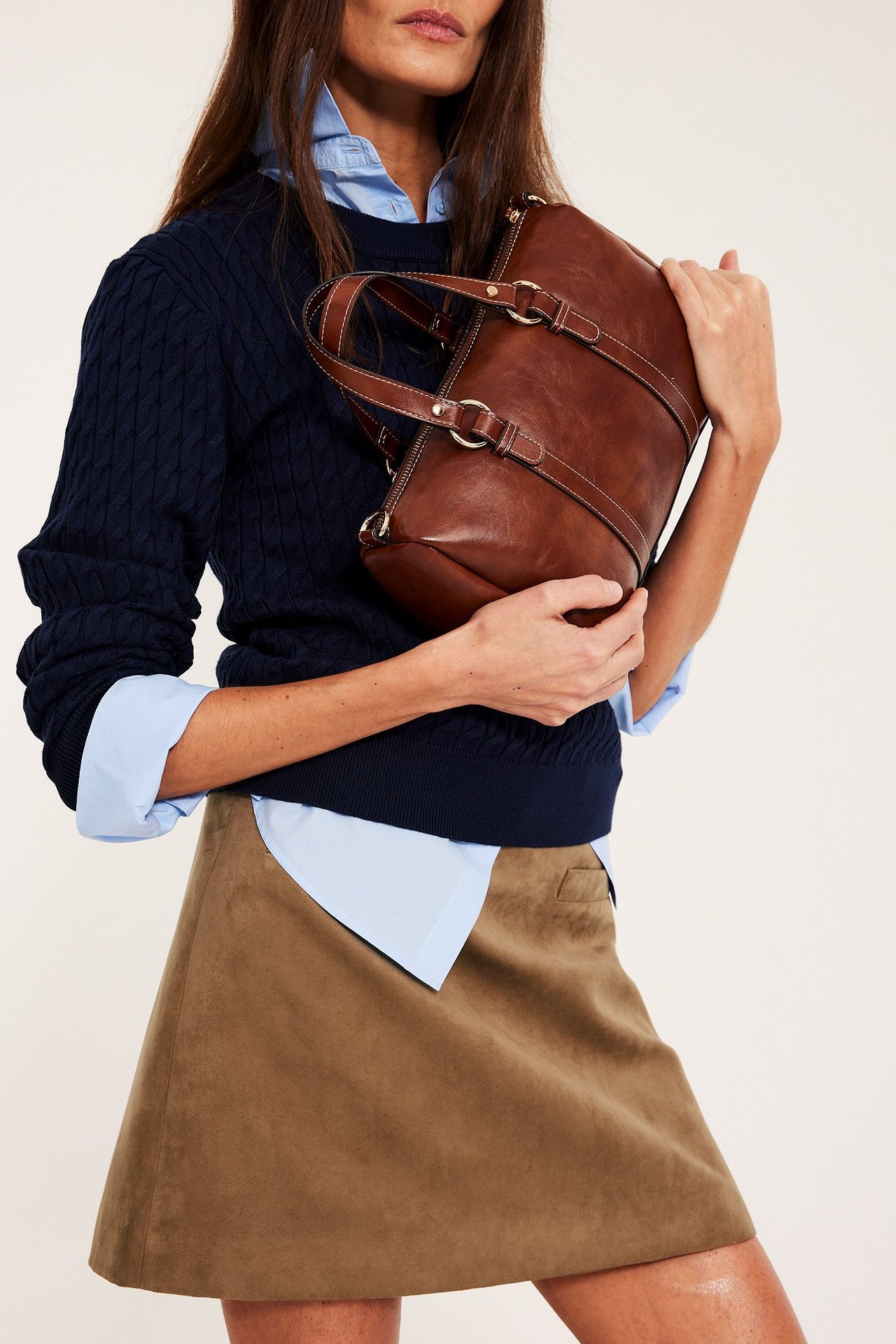 Framsida: kvinna i brun kort kjol i mockaimitation, marinblå tröja, ljusblå skjorta, håller brun väska.