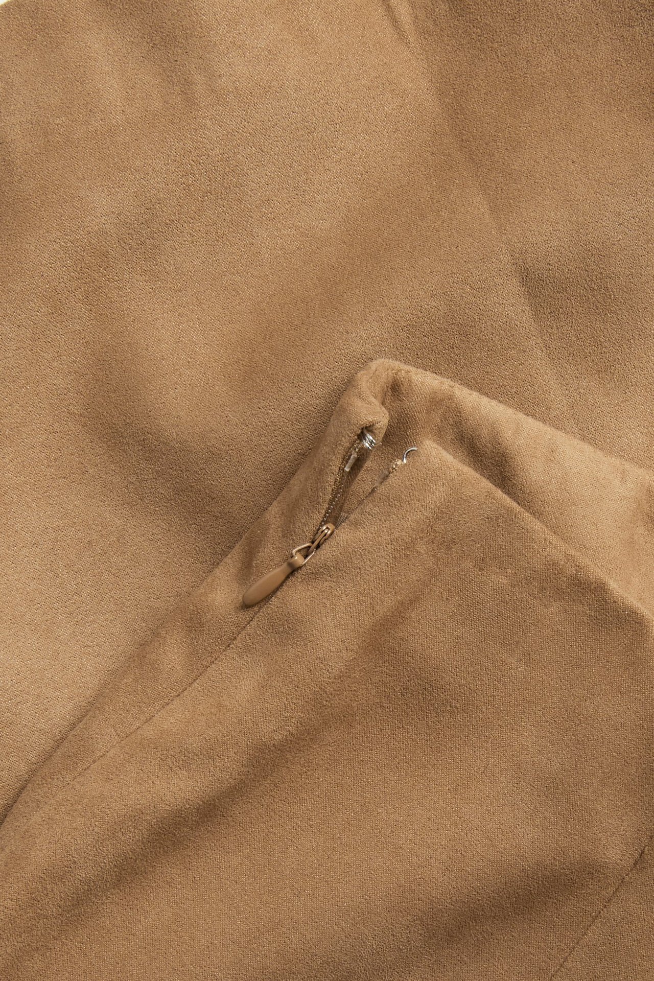 Nærbilde av et brunt kort skjørt i imitert skinn med glidelås i siden.