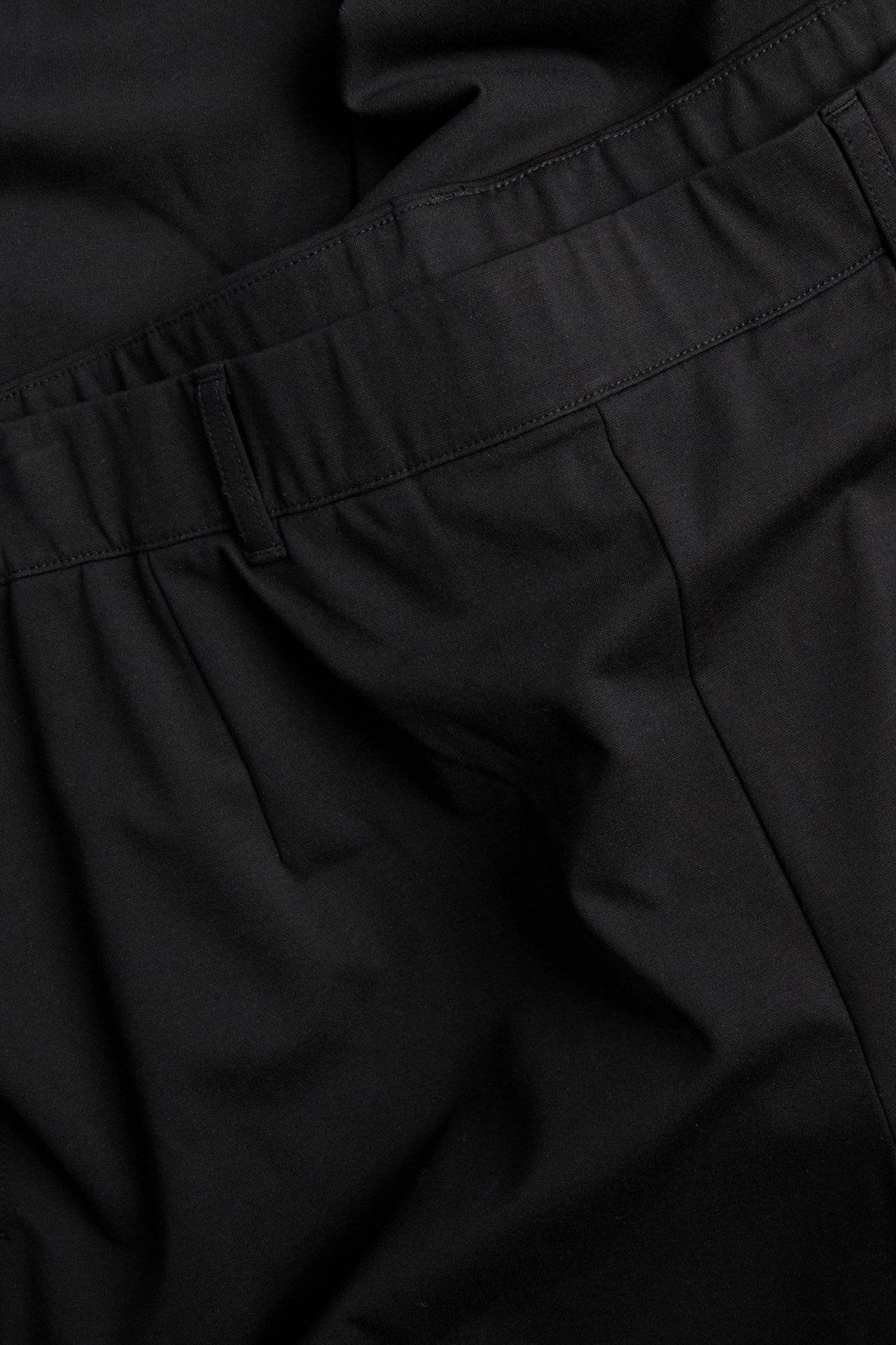 Widok z bliska z przodu czarnych, szerokich eleganckich spodni z paskiem i zakładkami.