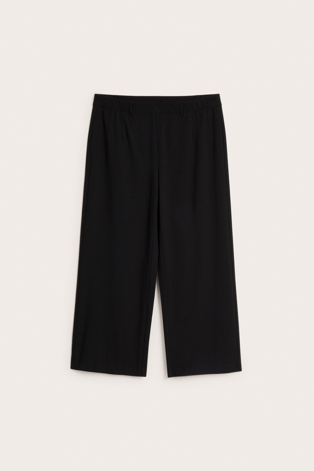 Edestäpäin näkymä mustista leveälahkeisista, vajaamittaisista puvunhousuista joustavalla vyötäröllä.