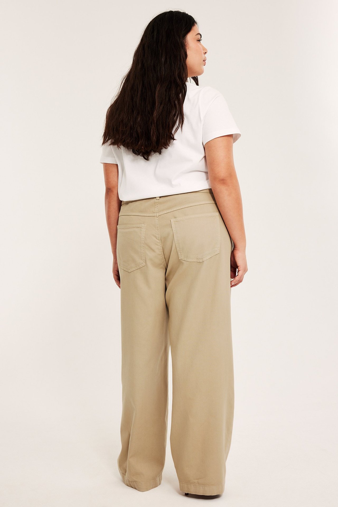 Bakfra, kvinne i beige vide bukser og en hvit t-skjorte.