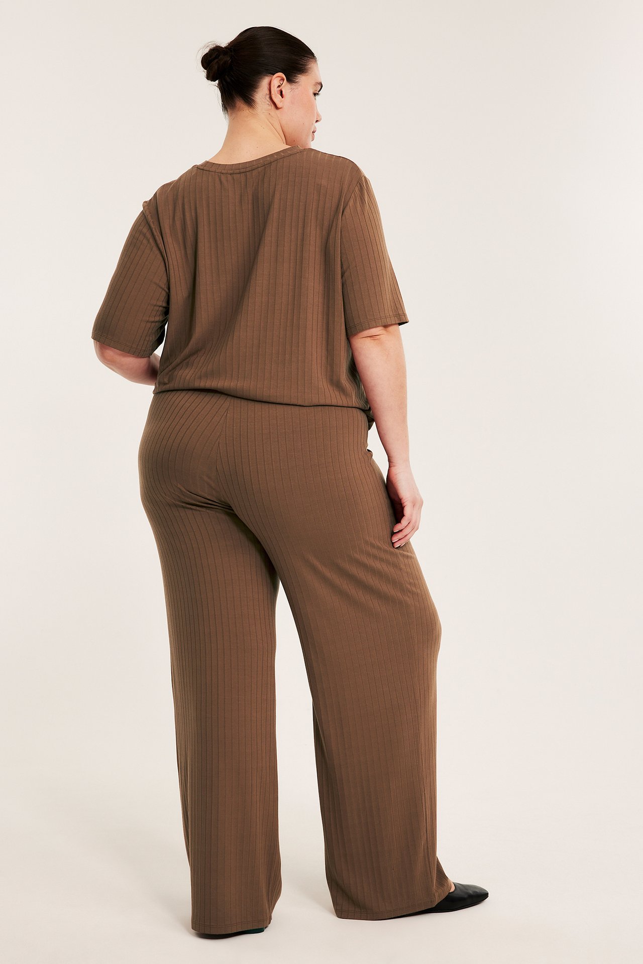 Widok z tyłu kobiety w brązowych, prążkowanych szerokich spodniach i pasującym krótkim topie.