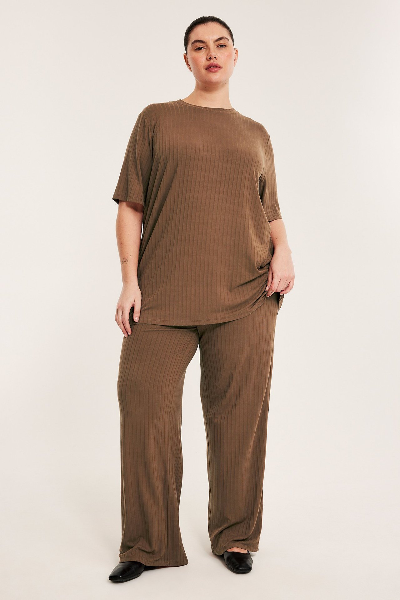 Framsida: kvinna i lösa bruna ribbade vida byxor, matchande topp och svarta skor.