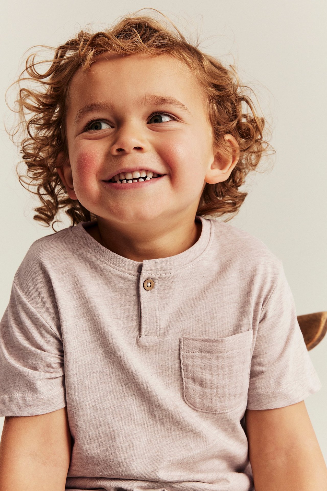 Nærbilde, forfra: Barn i melert beige kortermet T-skjorte med knappelukking og brystlomme.