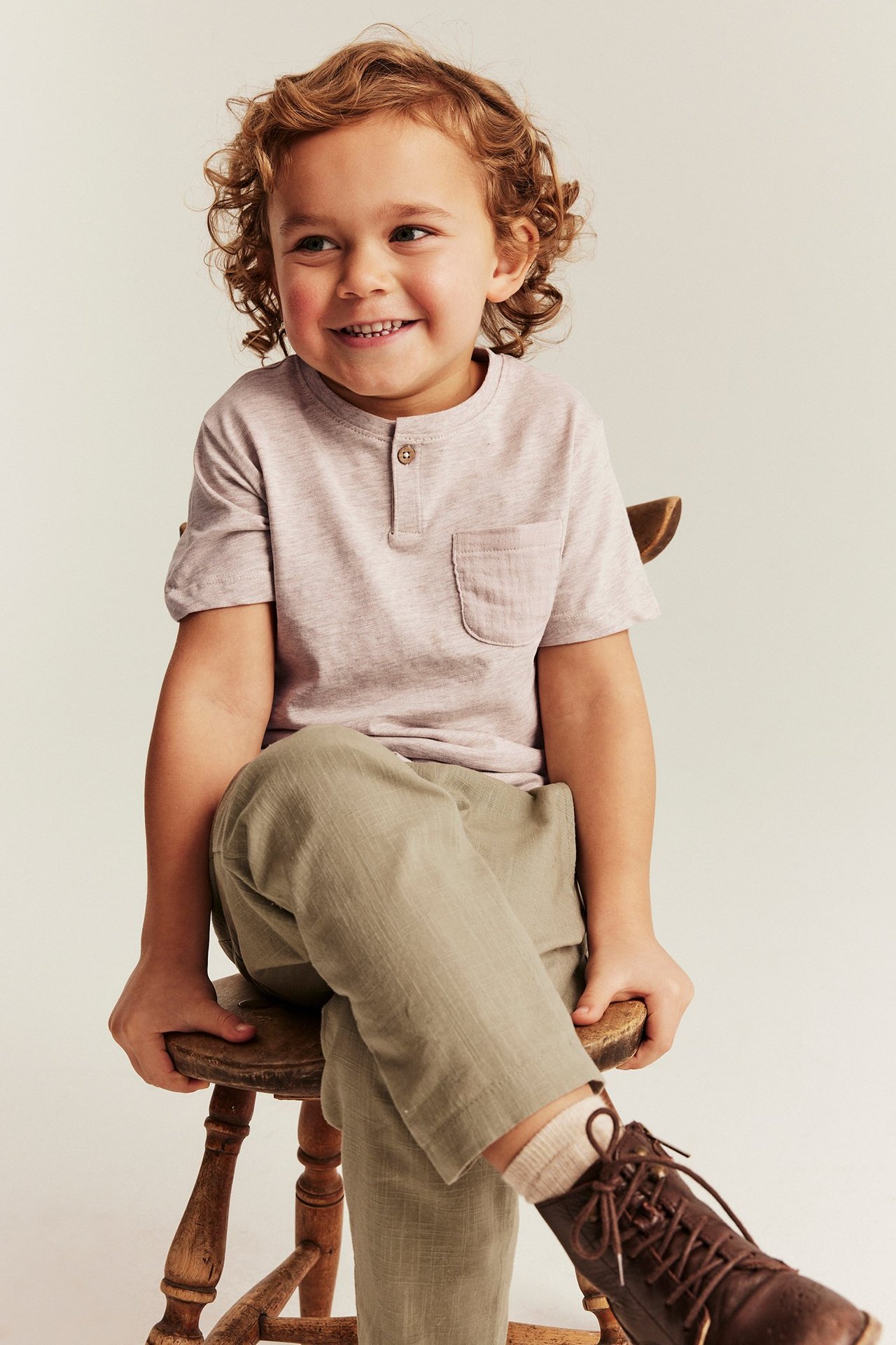 Widok z przodu: Dziecko ma na sobie beżowy melanżowy T-shirt z guzikami, kieszonką, oliwkowe spodnie, brązowe buty.