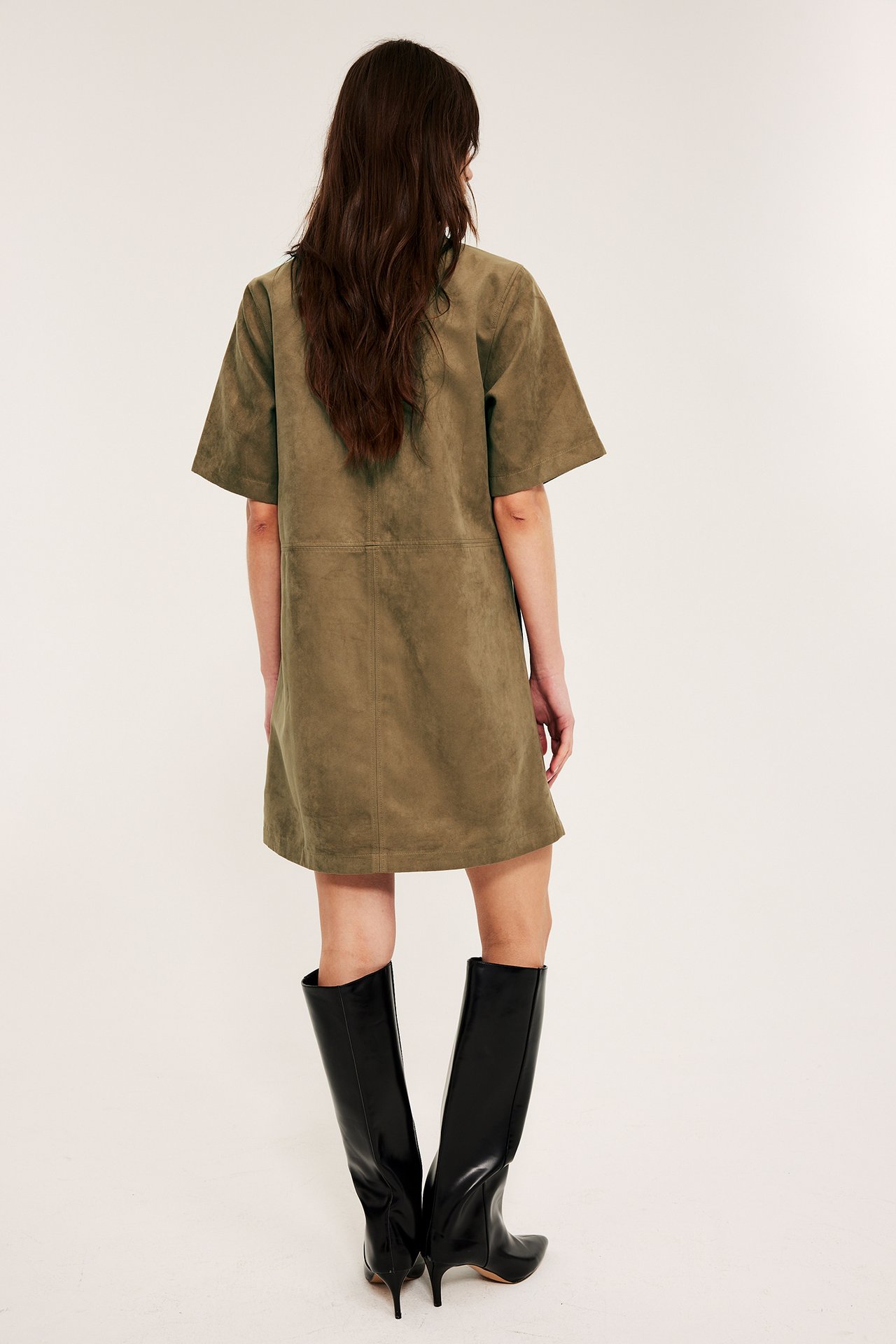 Takanäkymä naisesta, jolla on ruskea mokkajäljitelmä lyhyt mekko ja mustat polvisaappaat.