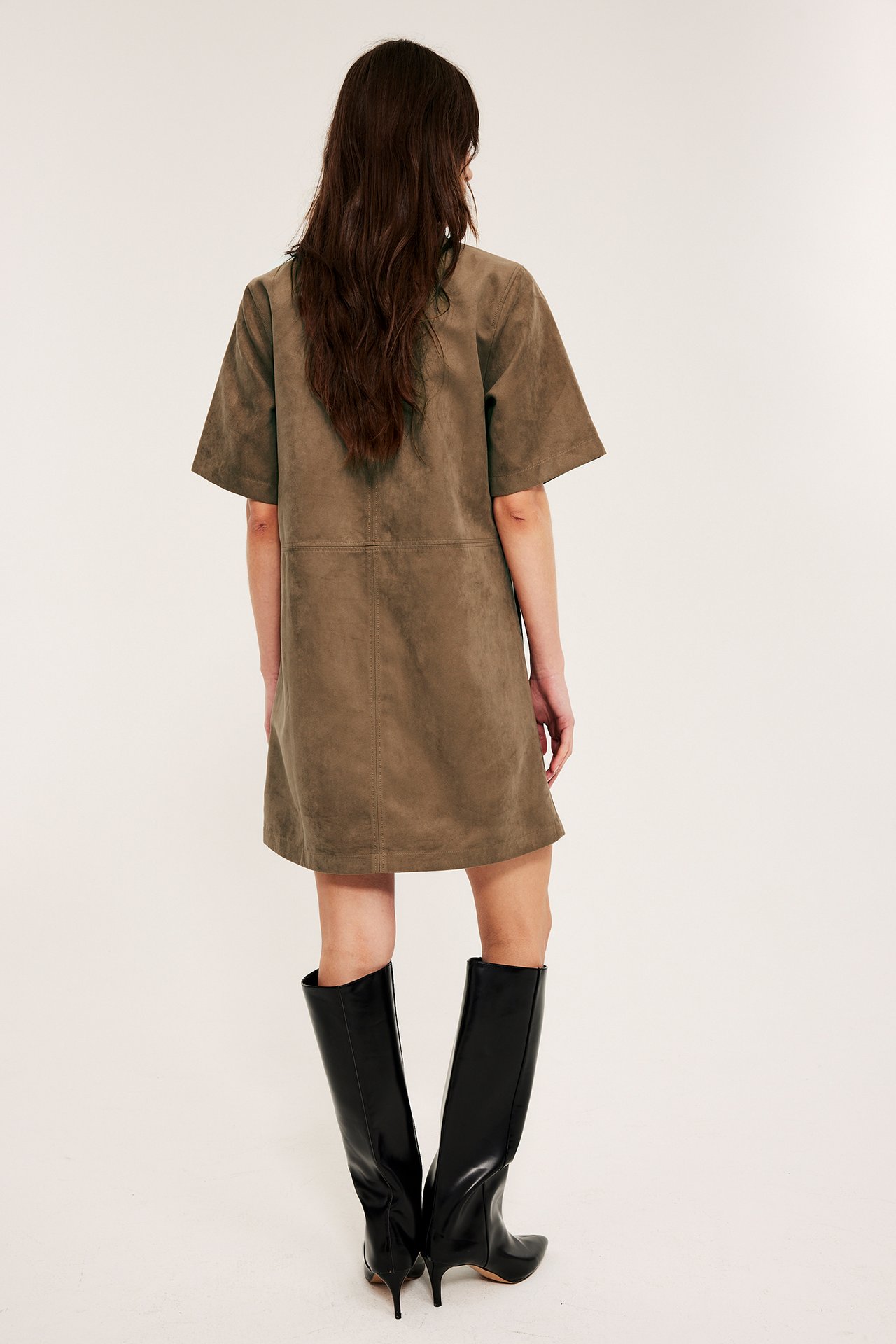 Bakifrån: Kvinna i kort brun klänning i mockaimitation med korta ärmar och svarta knähöga stövlar.