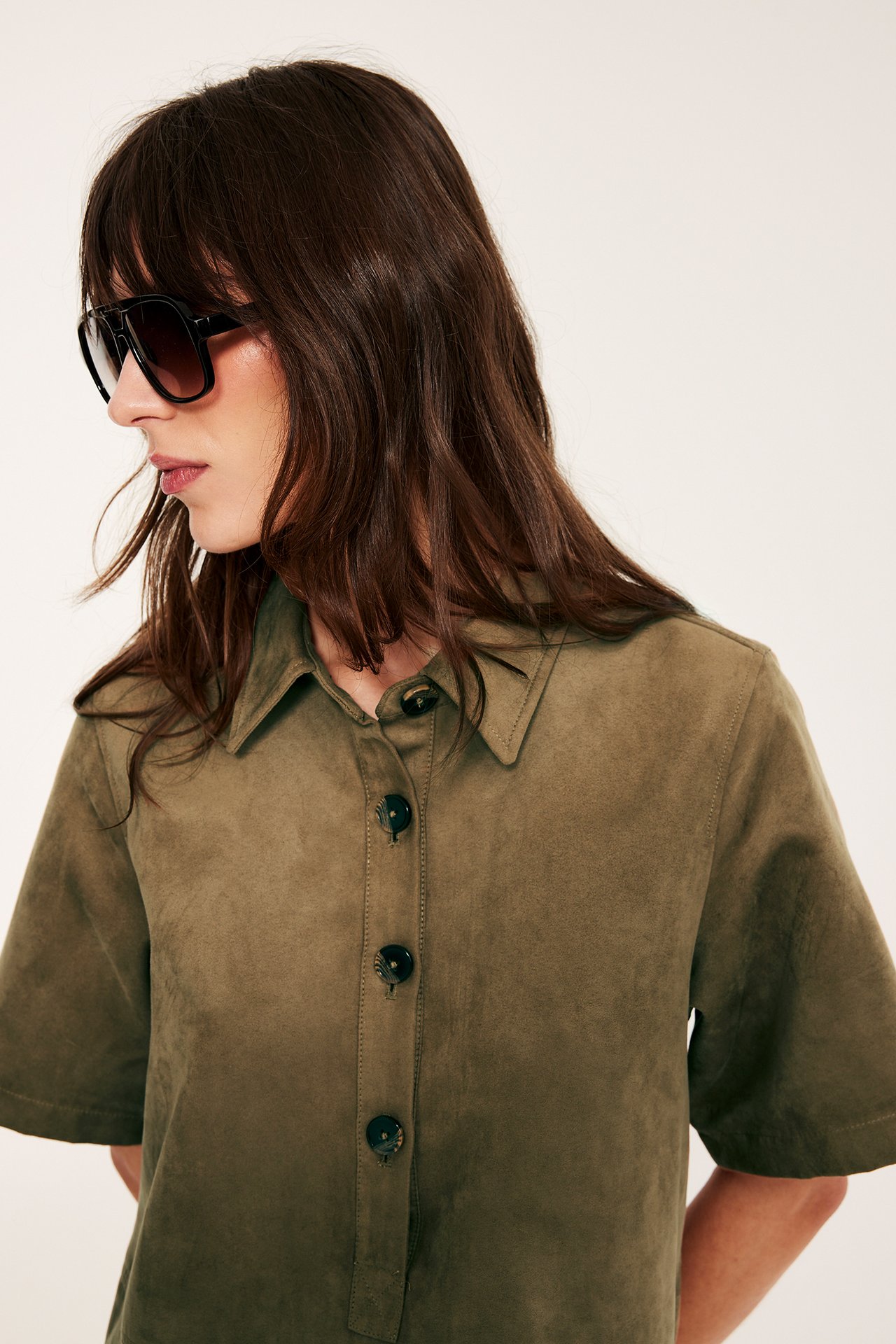 Sivukuva naisesta khakinruskeassa mokkajäljitelmä-minimekossa, jossa edessä napitus ja mustat aurinkolasit.