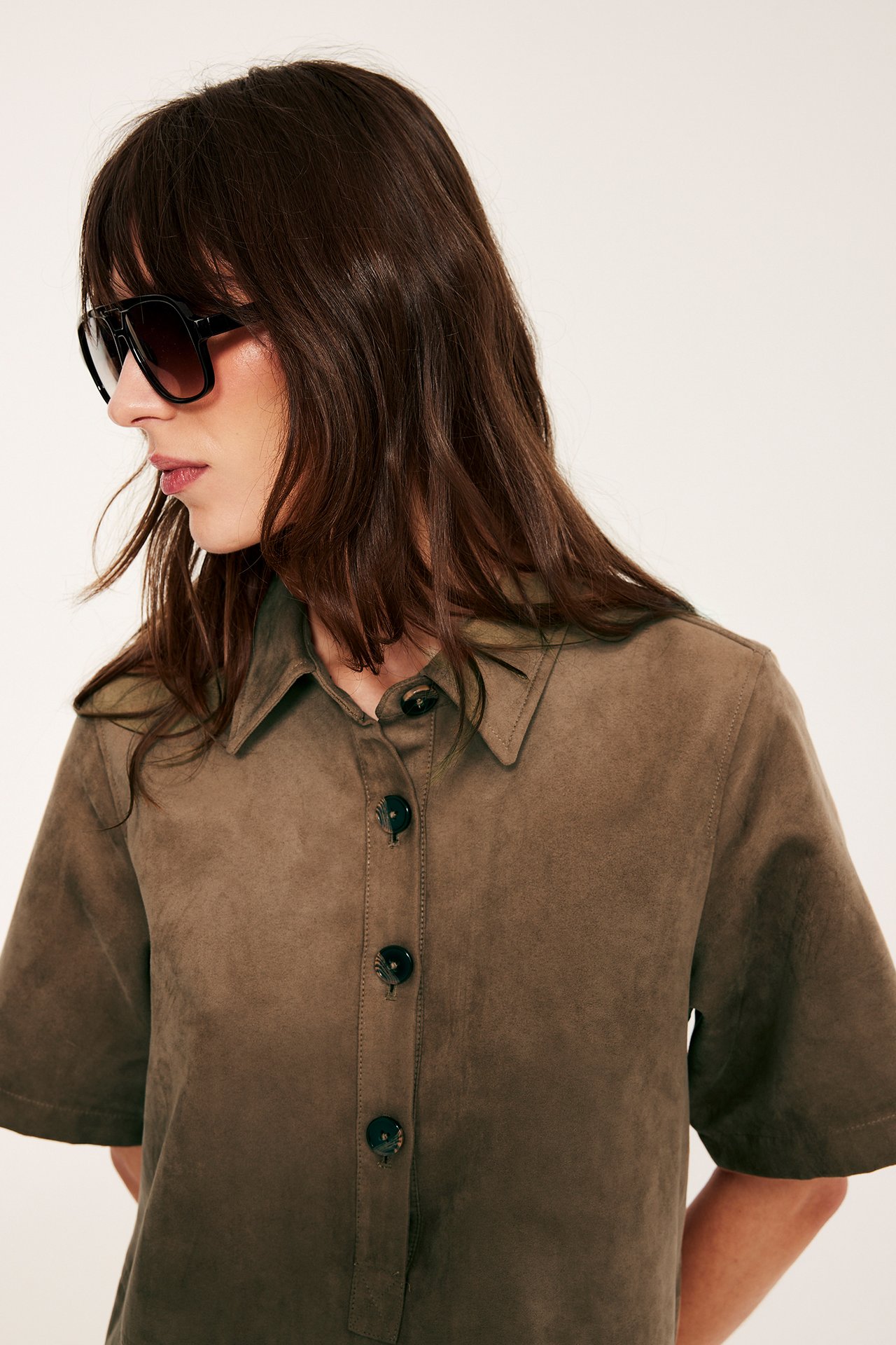 Sidovy av kvinna i brun kort klänning i mockaimitation med knappar fram och mörka solglasögon.