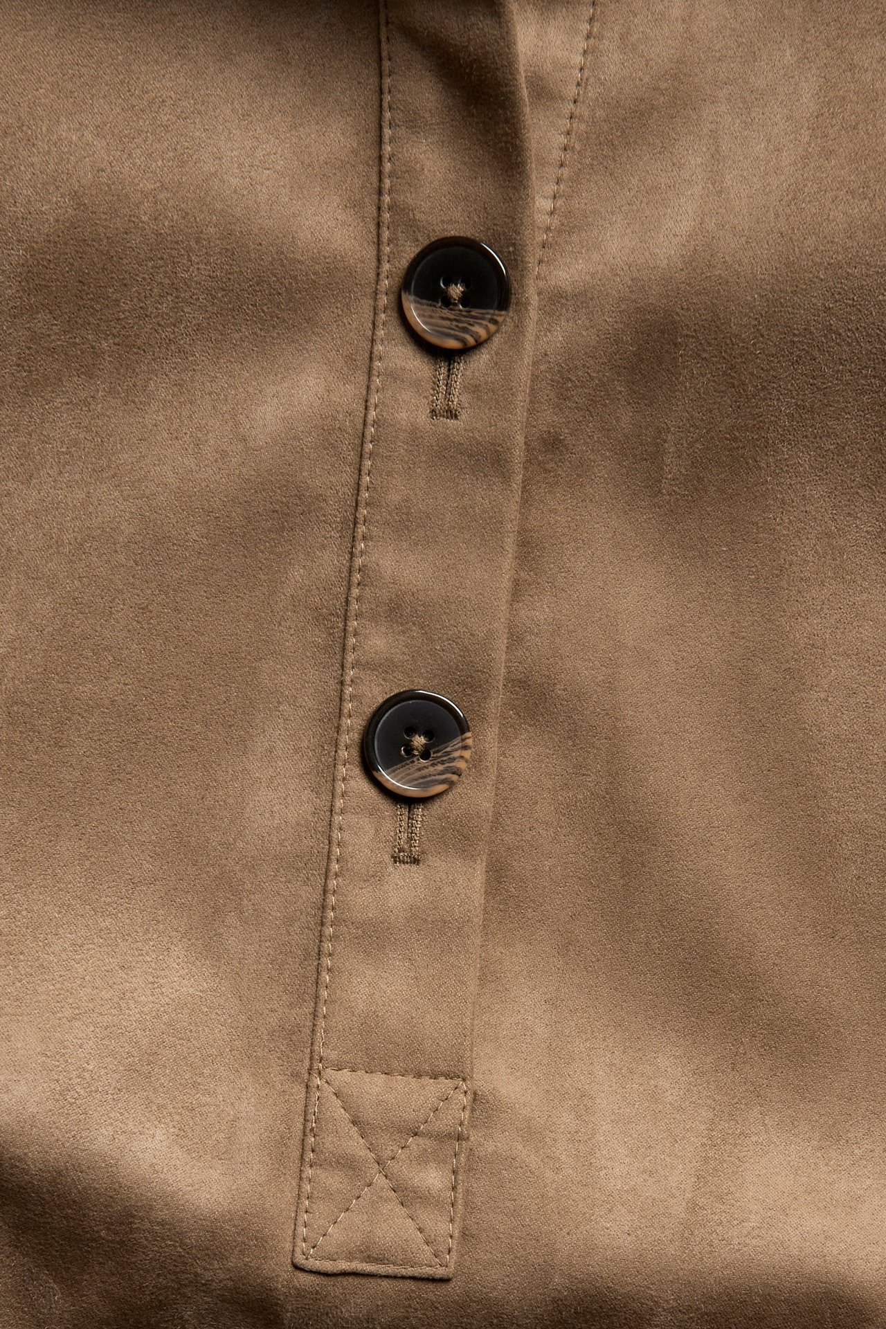 Närbild av en brun klänning i mockaimitation, med två mörka mönstrade knappar och synliga sömmar.