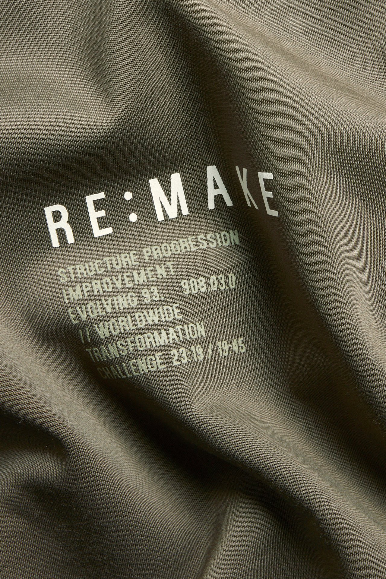 Zbliżenie na zieloną bluzę dresową interlock z białym napisem 'RE:MAKE'.