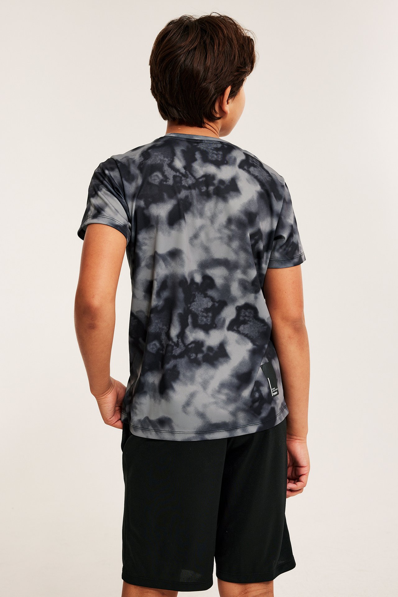 Widok od tyłu dziecka w czarno-szarej wzorzystej koszulce sportowej z krótkim rękawem i czarnych szortach.