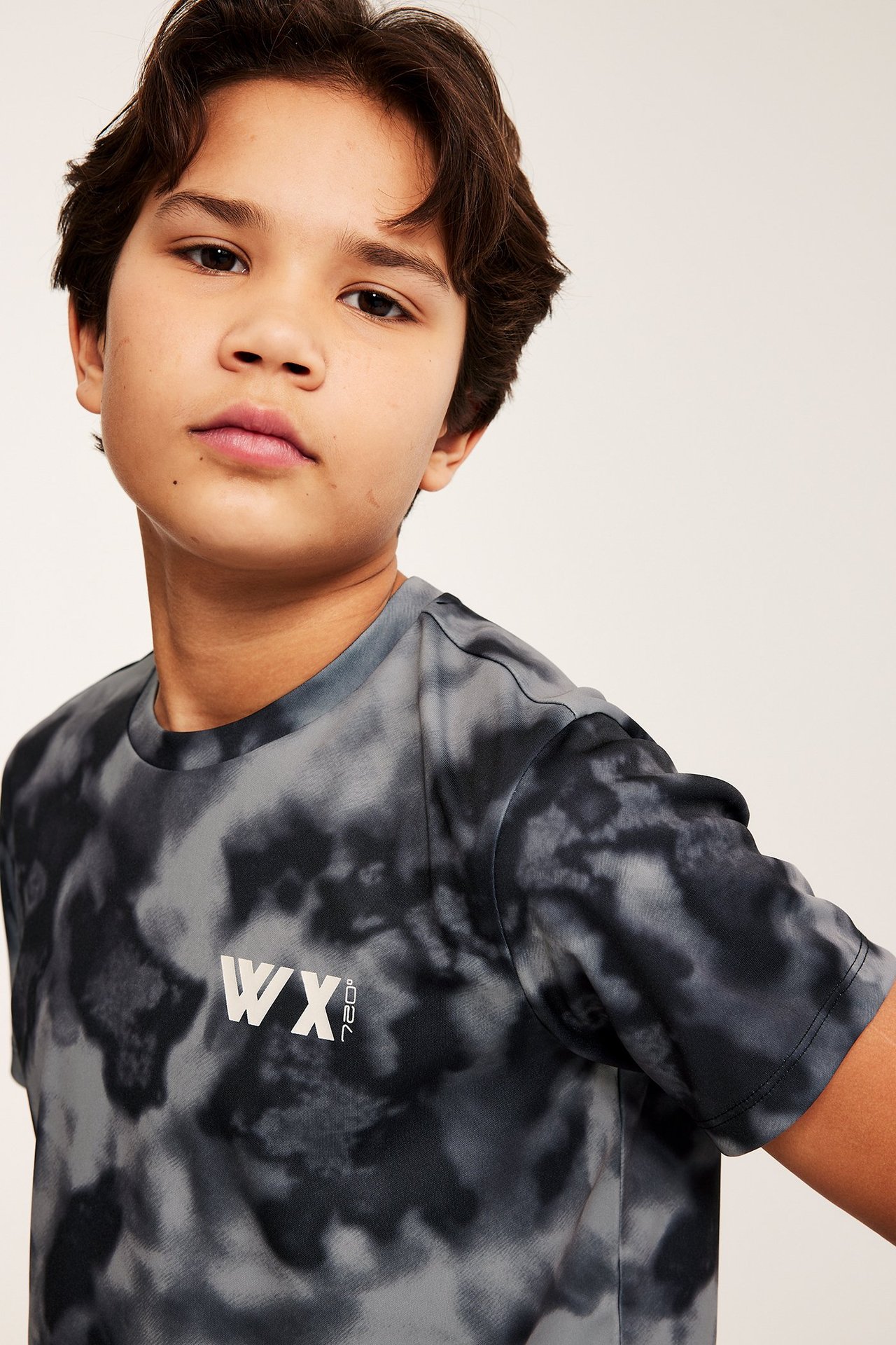 Widok z przodu, dziecko w czarno-szarej, wzorzystej koszulce sportowej z poliestru z białym logo.