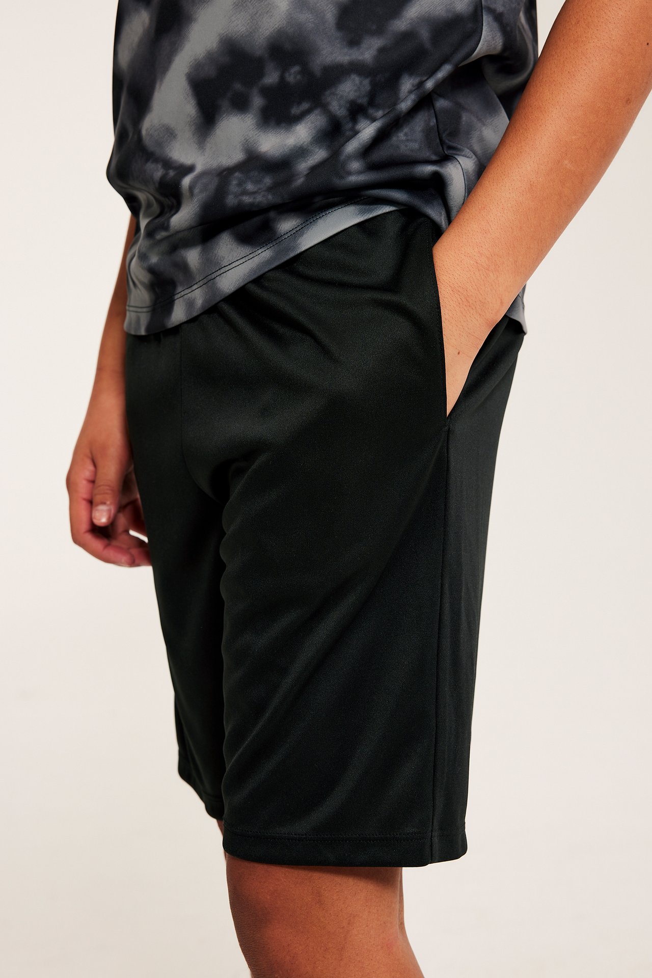 Widok z boku: czarne, gładkie szorty dla dziecka z ręką w kieszeni i wzorzysty top.