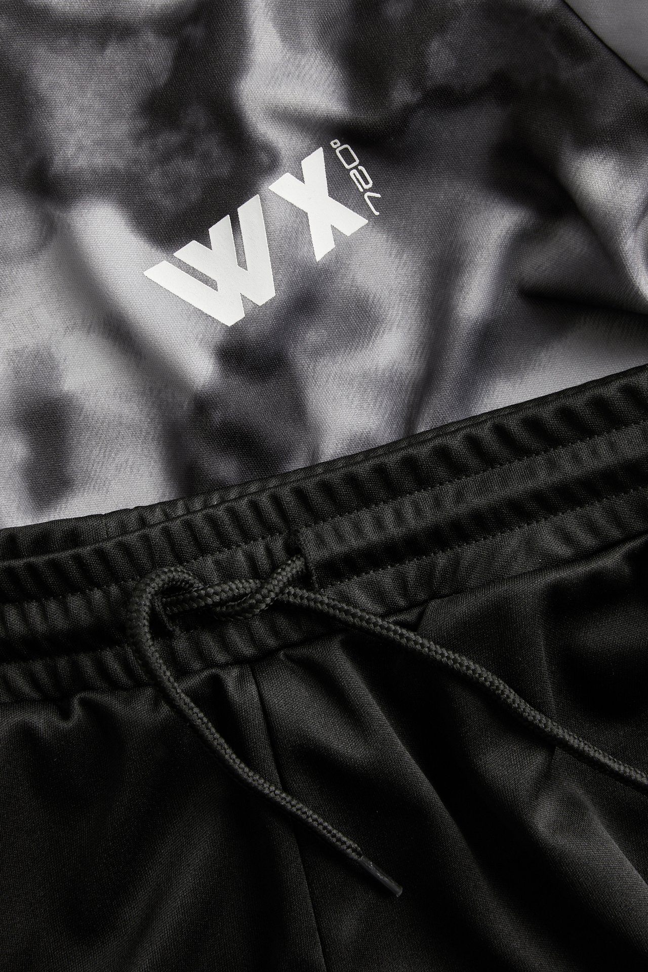 Zbliżenie: czarno-szary wzorzysty top sportowy z białym logo i czarne poliestrowe szorty ze sznurkiem.