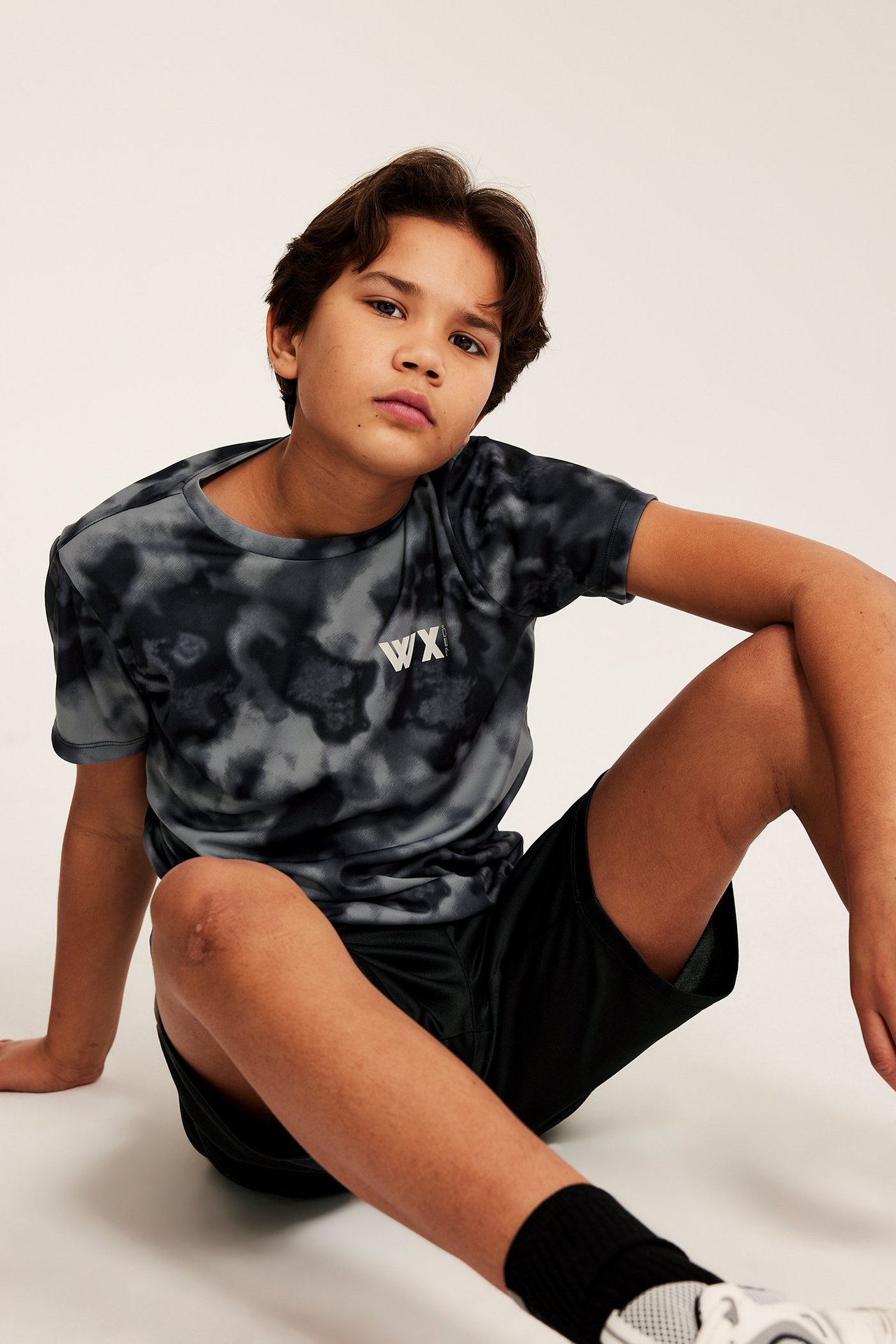 Chłopiec w czarnym zestawie sportowym, w wzorzystej T-shircie i gładkich szortach.