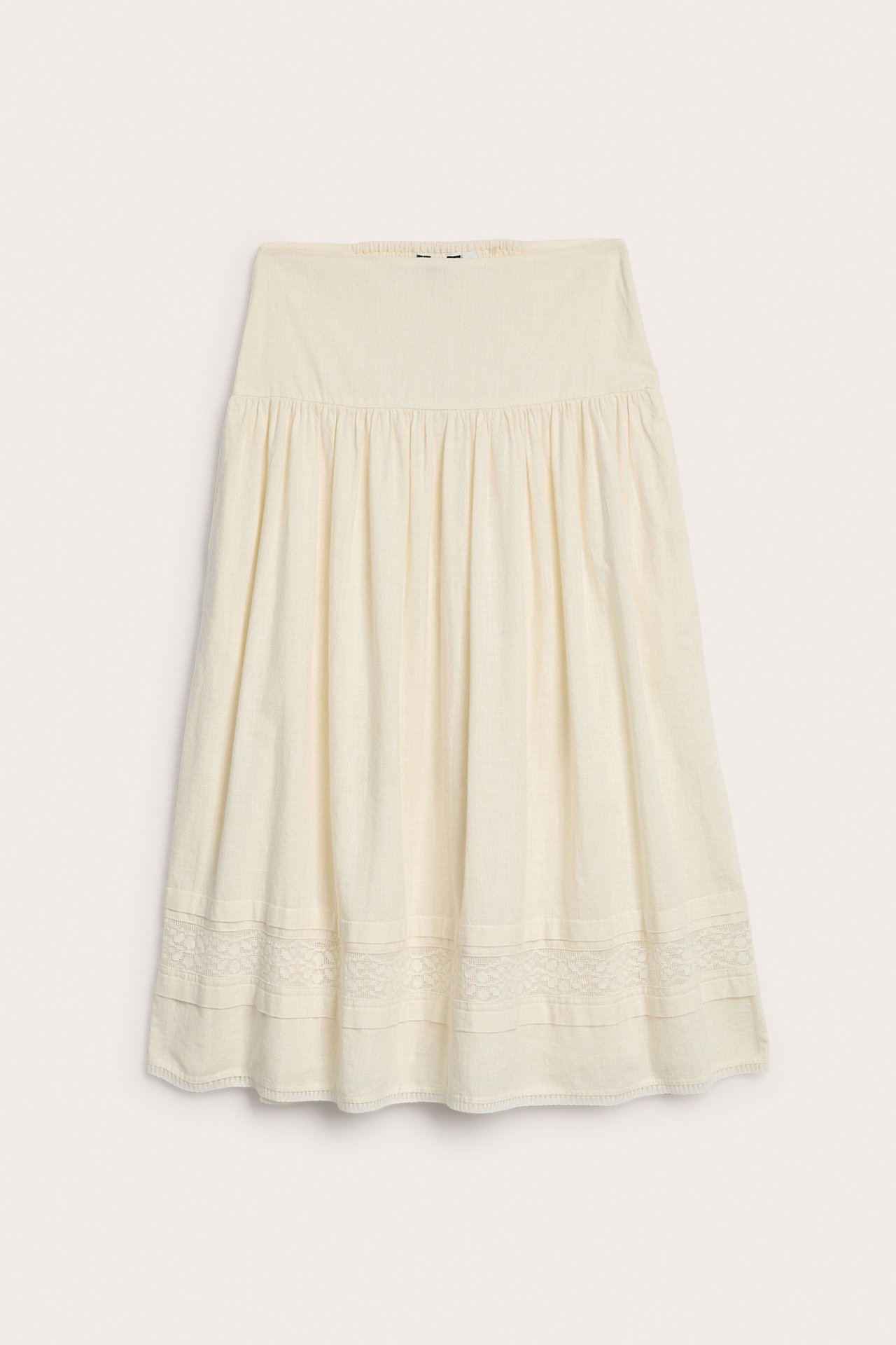 Widok z przodu kremowej bawełnianej spódnicy z marszczoną talią i koronkowymi detalami u dołu.
