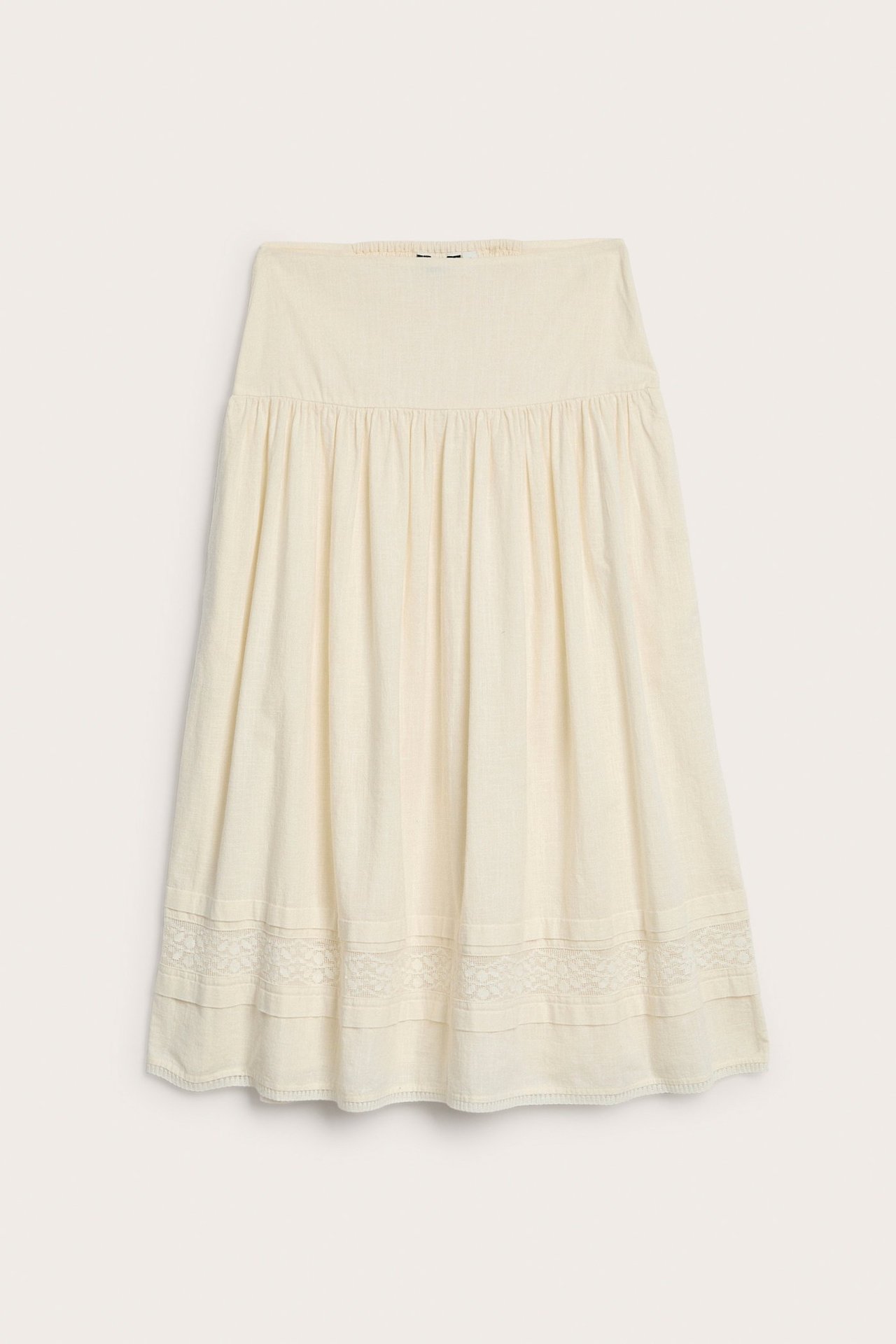 Edestä, luonnonvalkoinen puuvillahame, jossa smokkirypytys vyötäröllä ja pitsikoristelua helman lähellä.