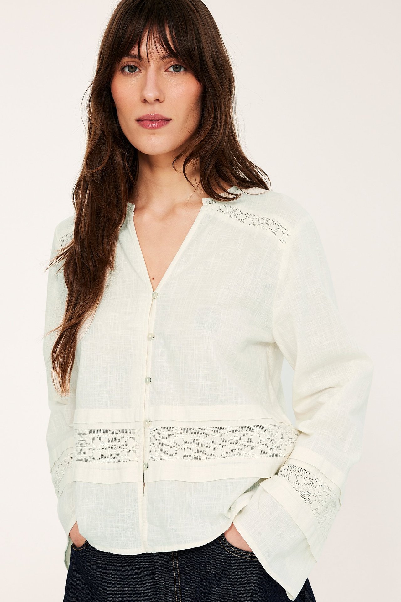 Widok z przodu kobiety w bluzce bawełnianej ecru z koronkowymi detalami i ciemnych dżinsach.