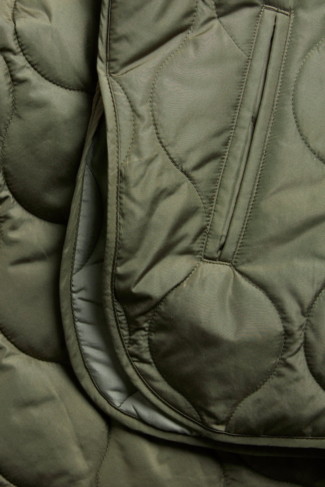 Zbliżenie zielonej pikowanej kurtki z falistym wzorem i widocznym rozcięciem z boku.