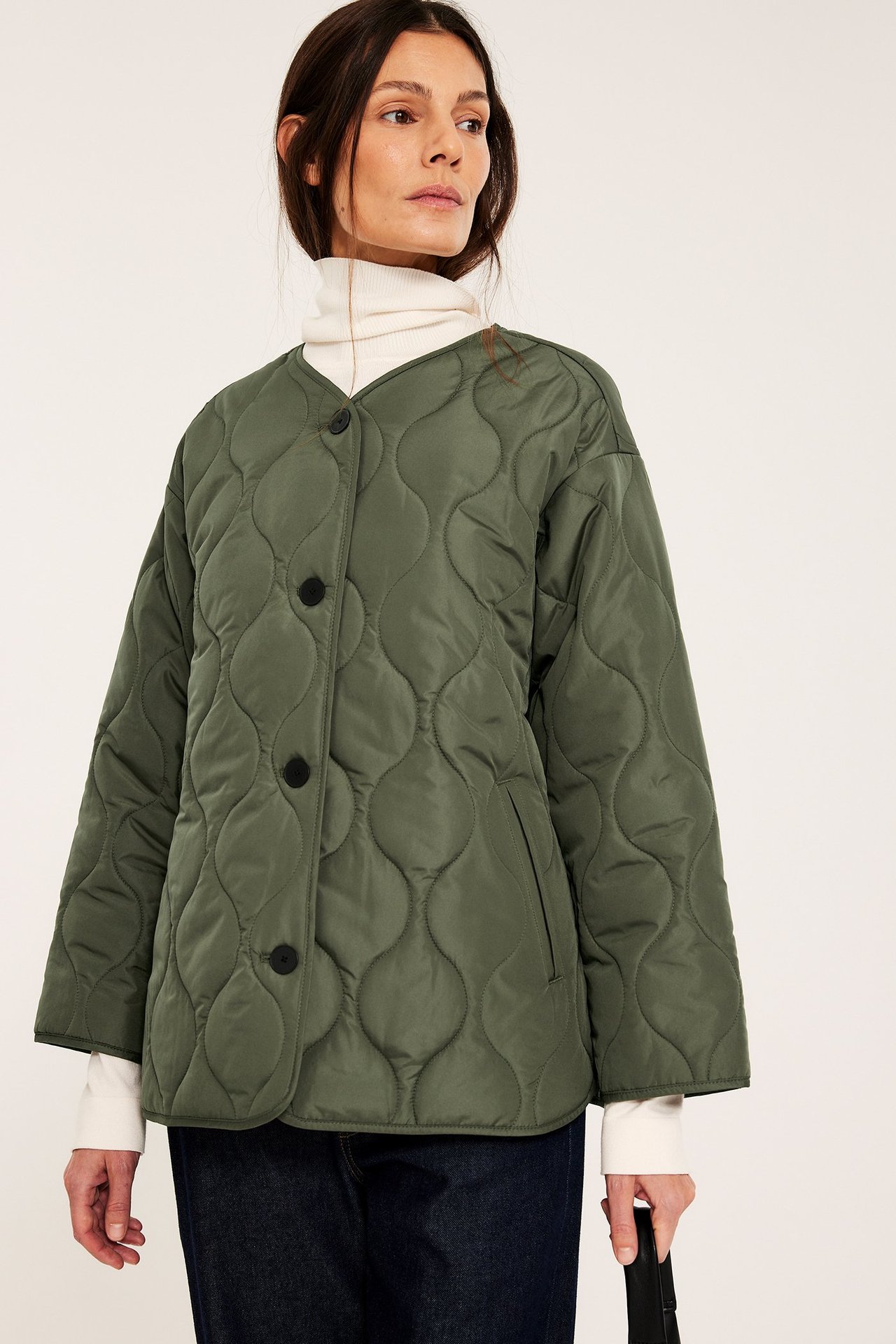 Nainen yllään vihreä tikattu takki mustilla napeilla, valkoisen poolon ja farkkujen päällä.