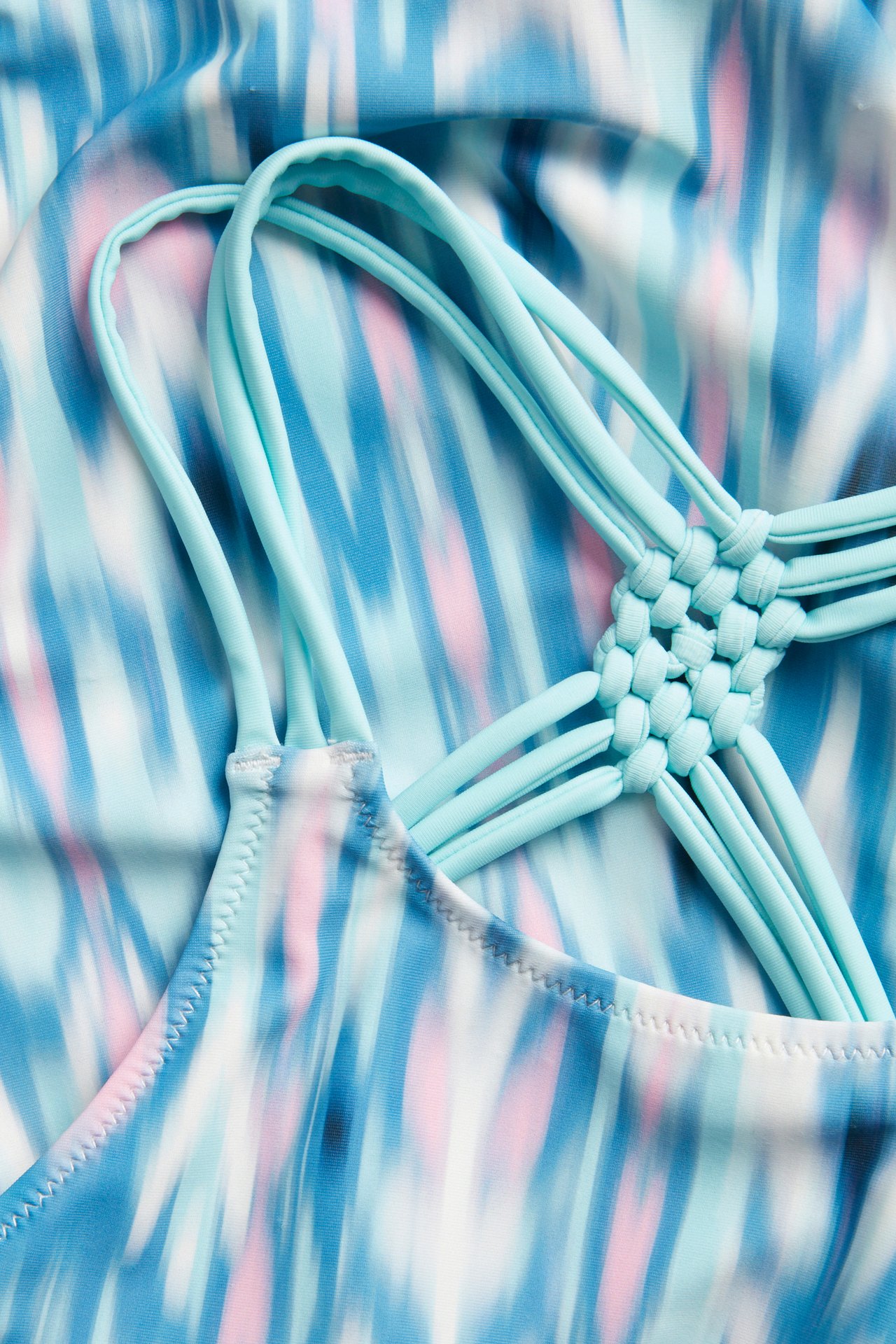 Nærbilde av en mønstret badedrakt for barn med abstrakte turkise, blå, rosa striper og flettede stropper.