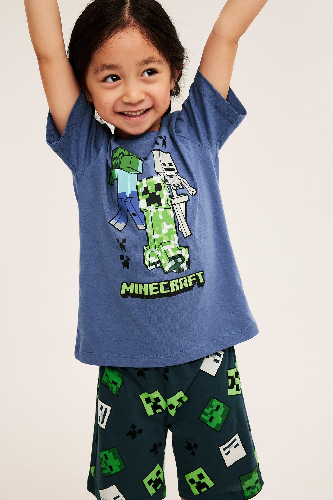 Edestä, lapsi sinisessä puuvillaisessa Minecraft-t-paidassa ja tummanvihreissä kuvioiduissa shortseissa.