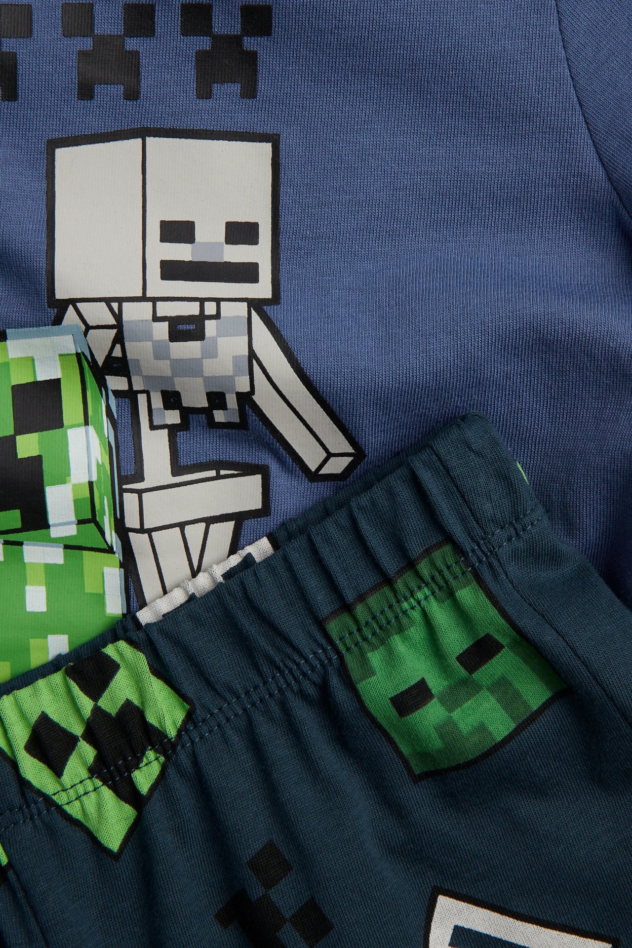 Närbild av ett blått pyjamasset i bomull för barn med Minecraft-skeletttryck på tröjan och mönstrade shorts.