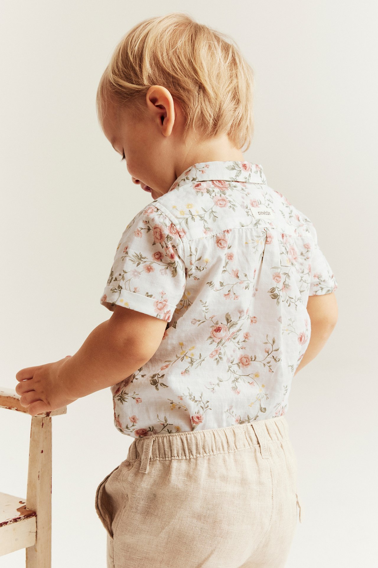 Bakfra-visning av et barn i offwhite blomstret kortermet bomulls-skjortebody og beige linstoffbukse.