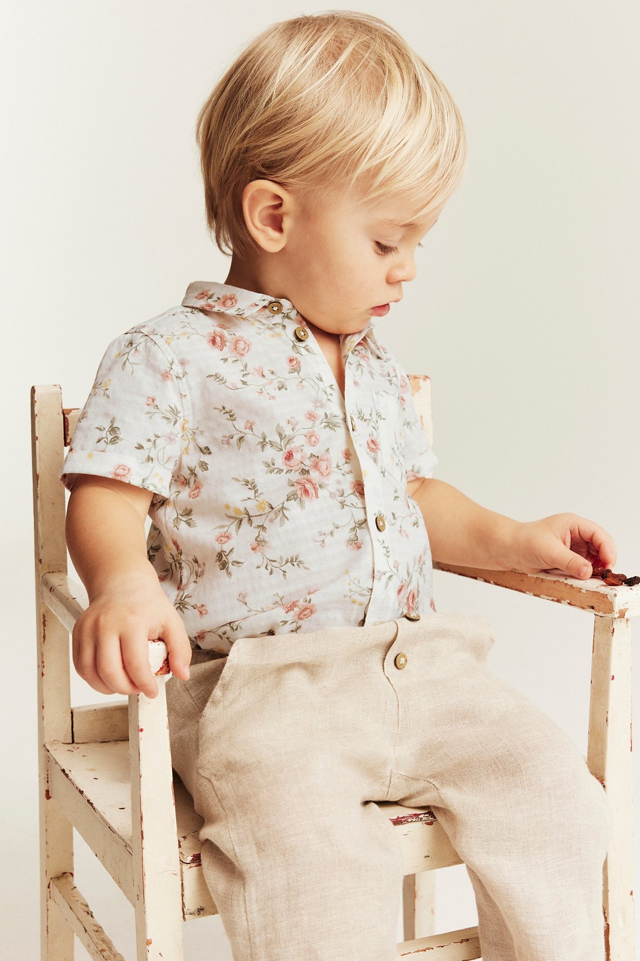 Widok z boku chłopca w ecru, kwiecistym, bawełnianym, krótkim body koszulowym i beżowych spodniach.