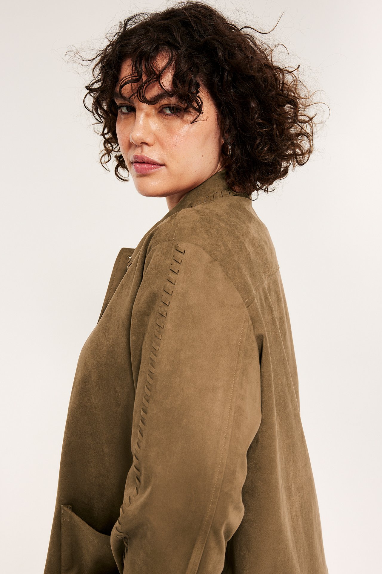 Sidovy av en kvinna i brun jacka i mockaimitation med dekorativa sömmar på krage och ärmar.