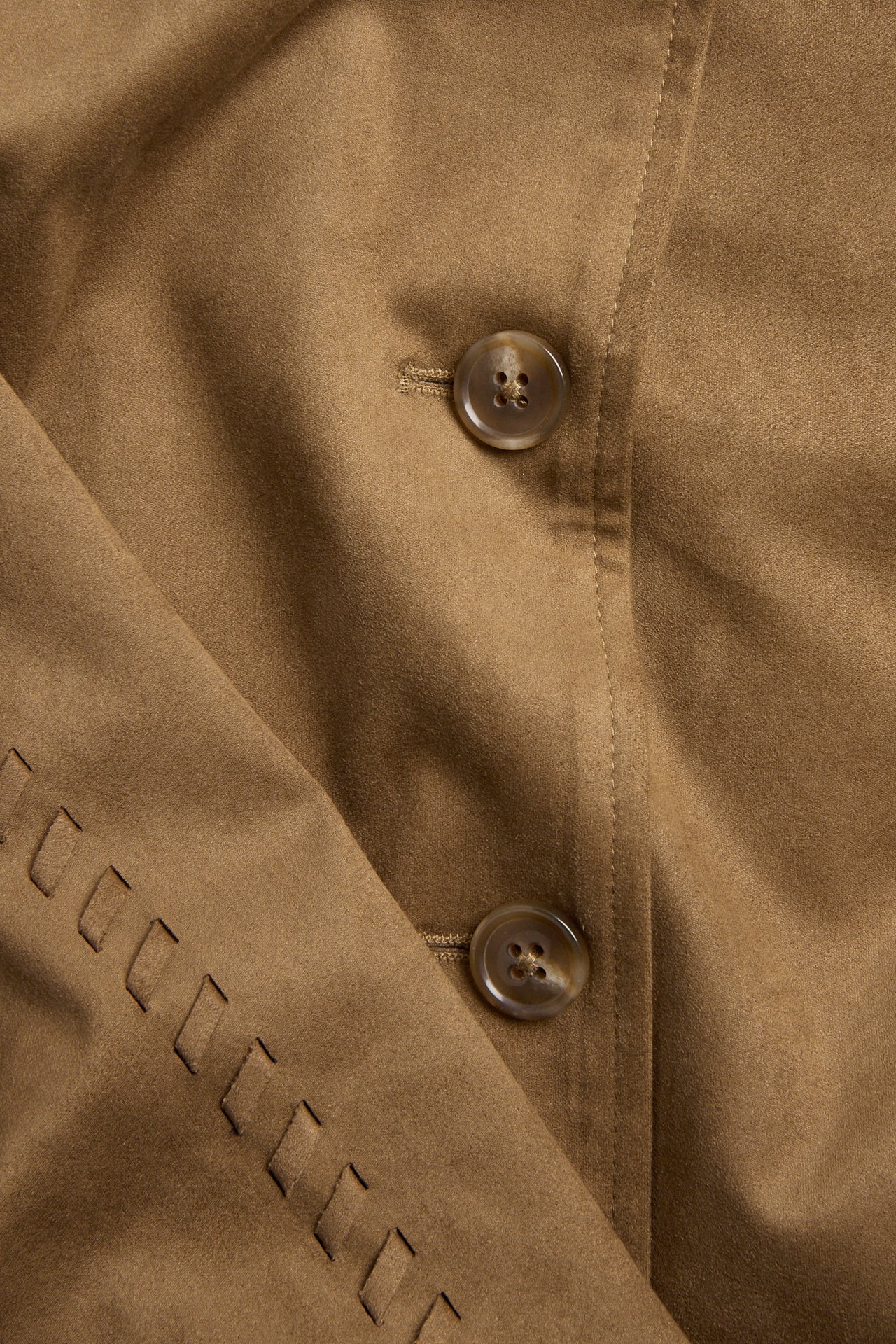 Närbild av en brun jacka i mockaimitation med två knappar och dekorativ utskuren söm.