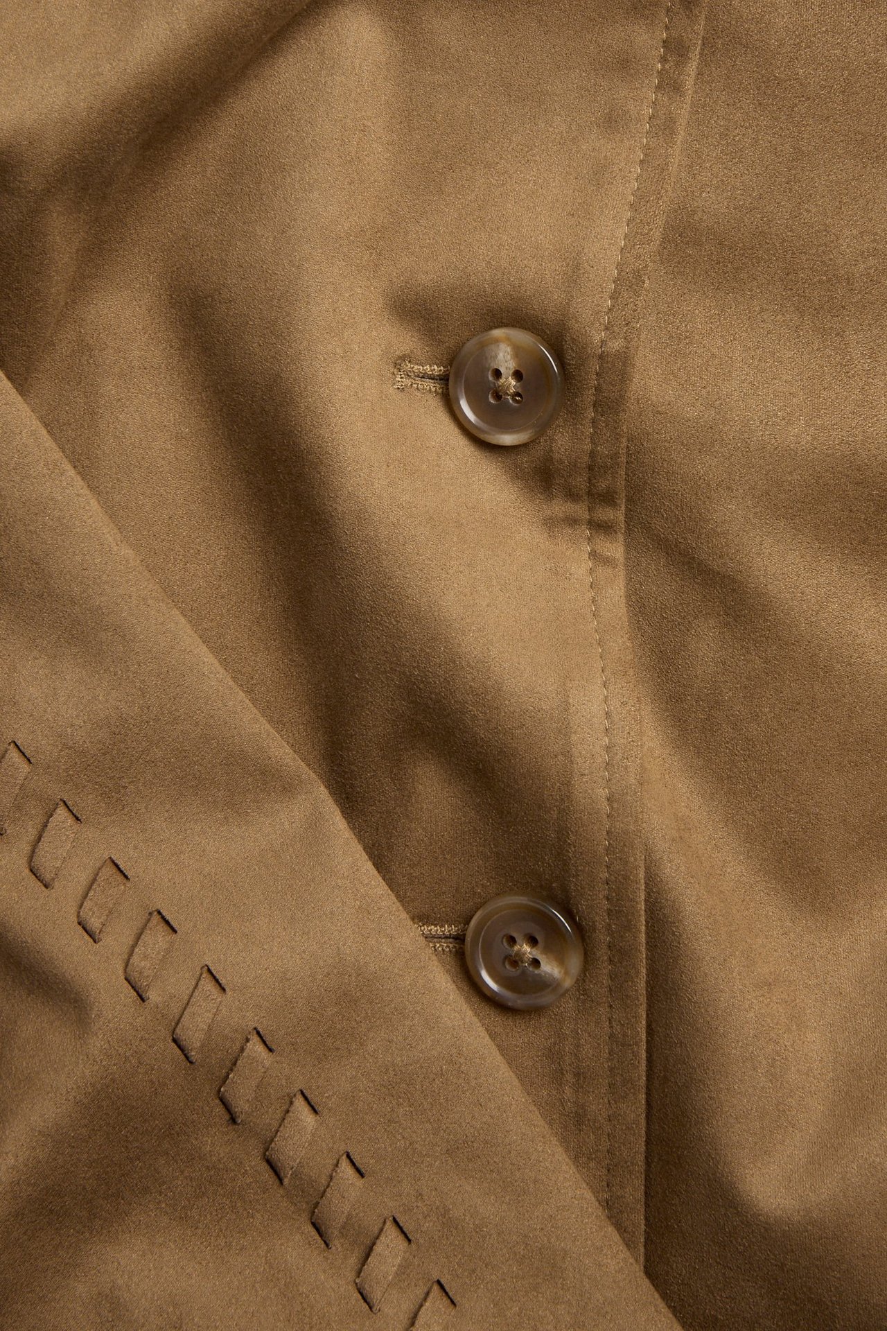 Zbliżenie brązowej kurtki ze sztucznego zamszu z dwoma guzikami i ozdobnymi wycięciami.