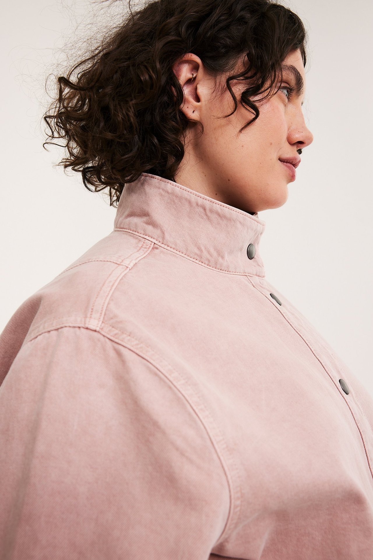 Lähikuva sivulta naisesta vaaleanpunaisessa puuvillatakissa, jossa on korkea kaulus ja tummat painonapit.