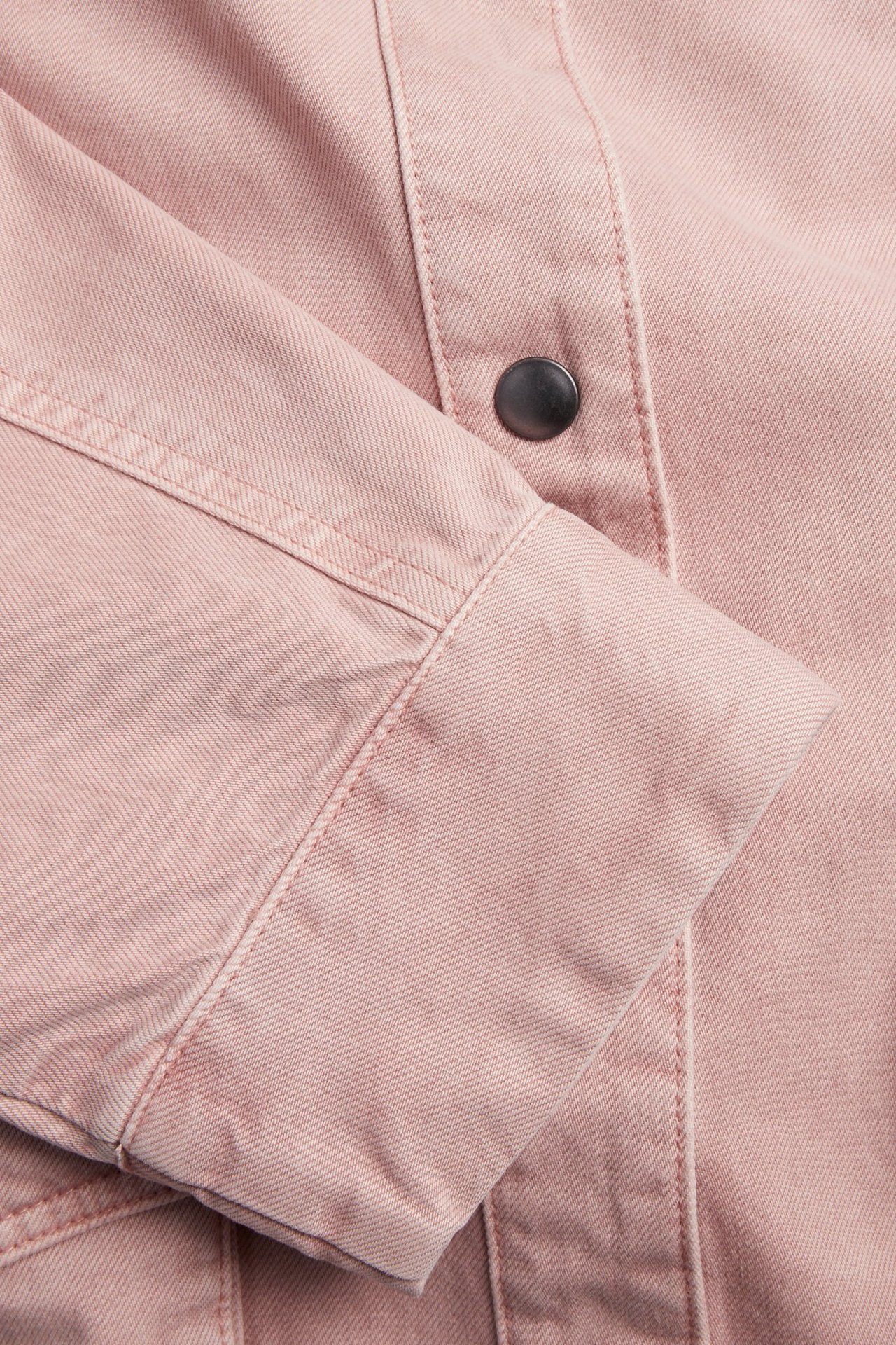 Närbild på en rosa bomullsjackas ärm och manschett med synliga sömmar och en mörk knapp.